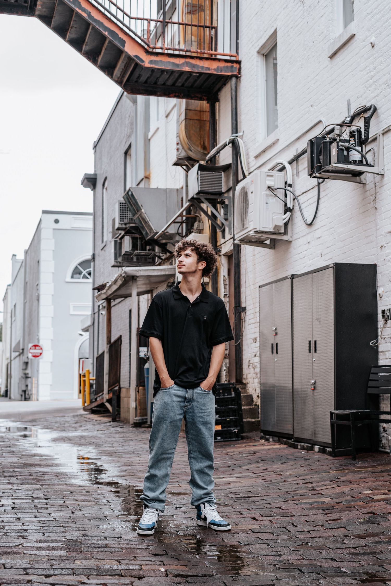 Person in black shirt and jeans walks on cobblestone street between white buildings in urban setting in downtown lakeland at Lake Mirror.