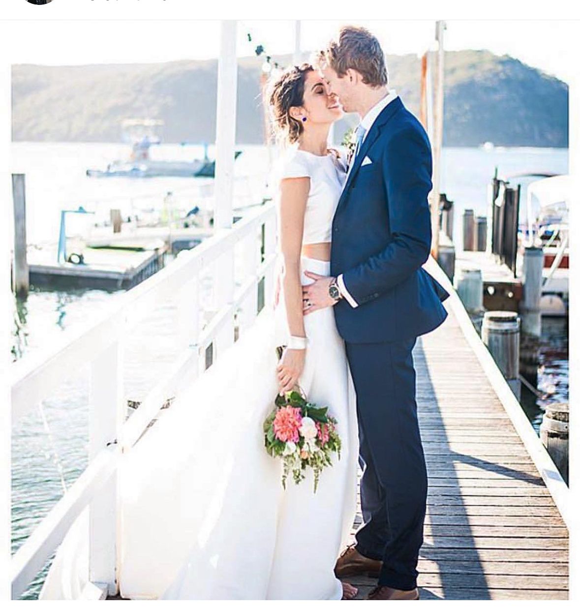 A couple shares an intimate moment on a waterfront dock during their wedding celebration.