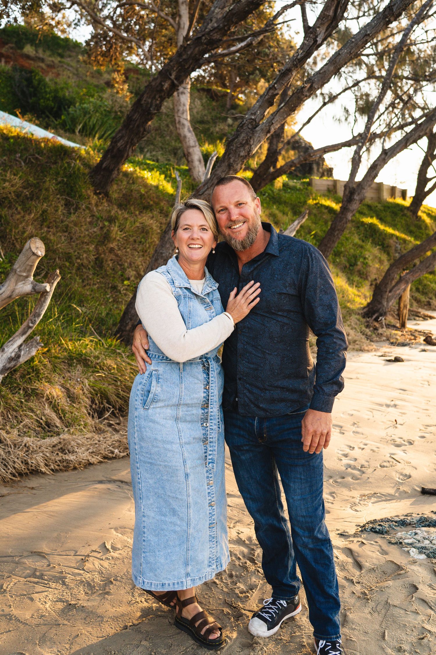 Happy middle-aged couple embracing and smiling together on a sandy beach at sunset.