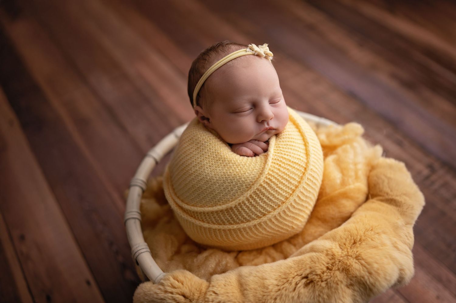 A sleeping newborn baby wearing a yellow knit wrap nestled in cozy yellow blankets for a professional portrait session.