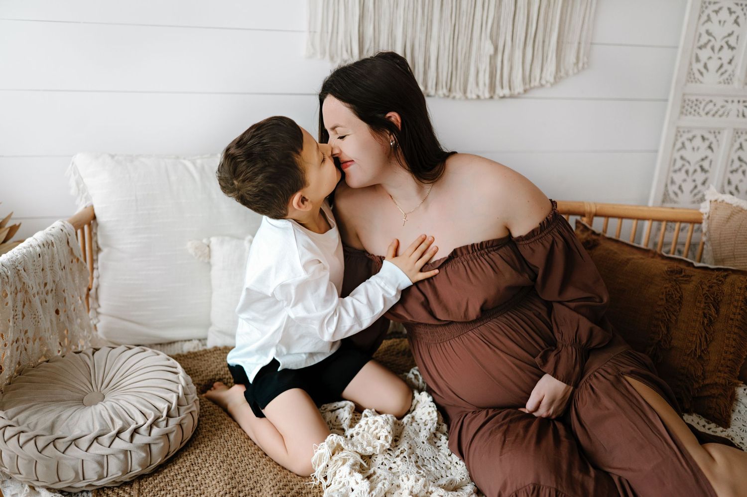 A romantic couple shares tender moments in a cozy bedroom with neutral decor and macrame wall hangings.