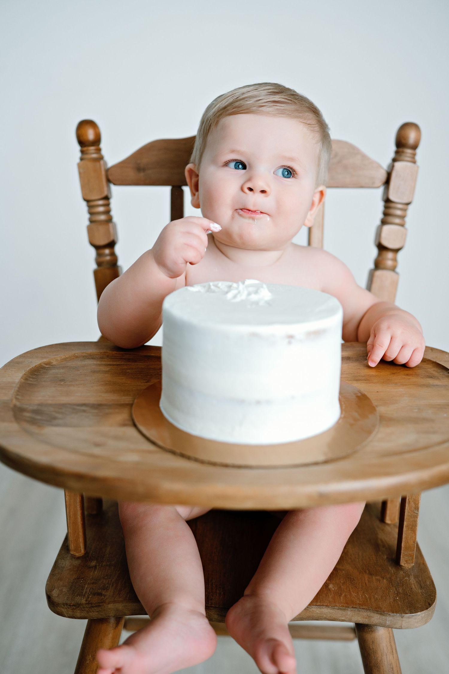 A sequence of photos showing a baby in a wooden high chair reaching towards a white cake on a rustic wooden tray.