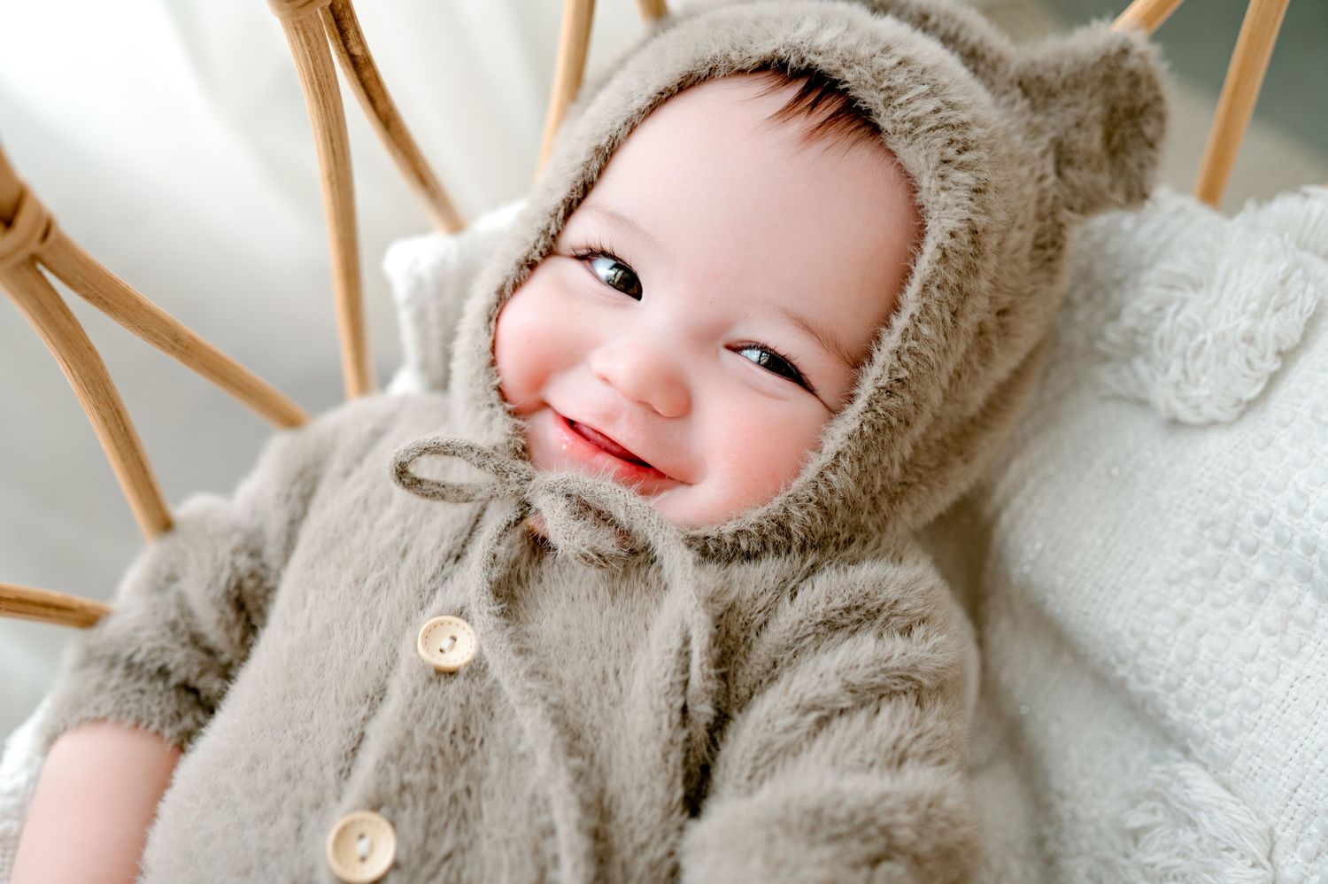 Close-up of baby in bear ear hoodie smiling against bright background.