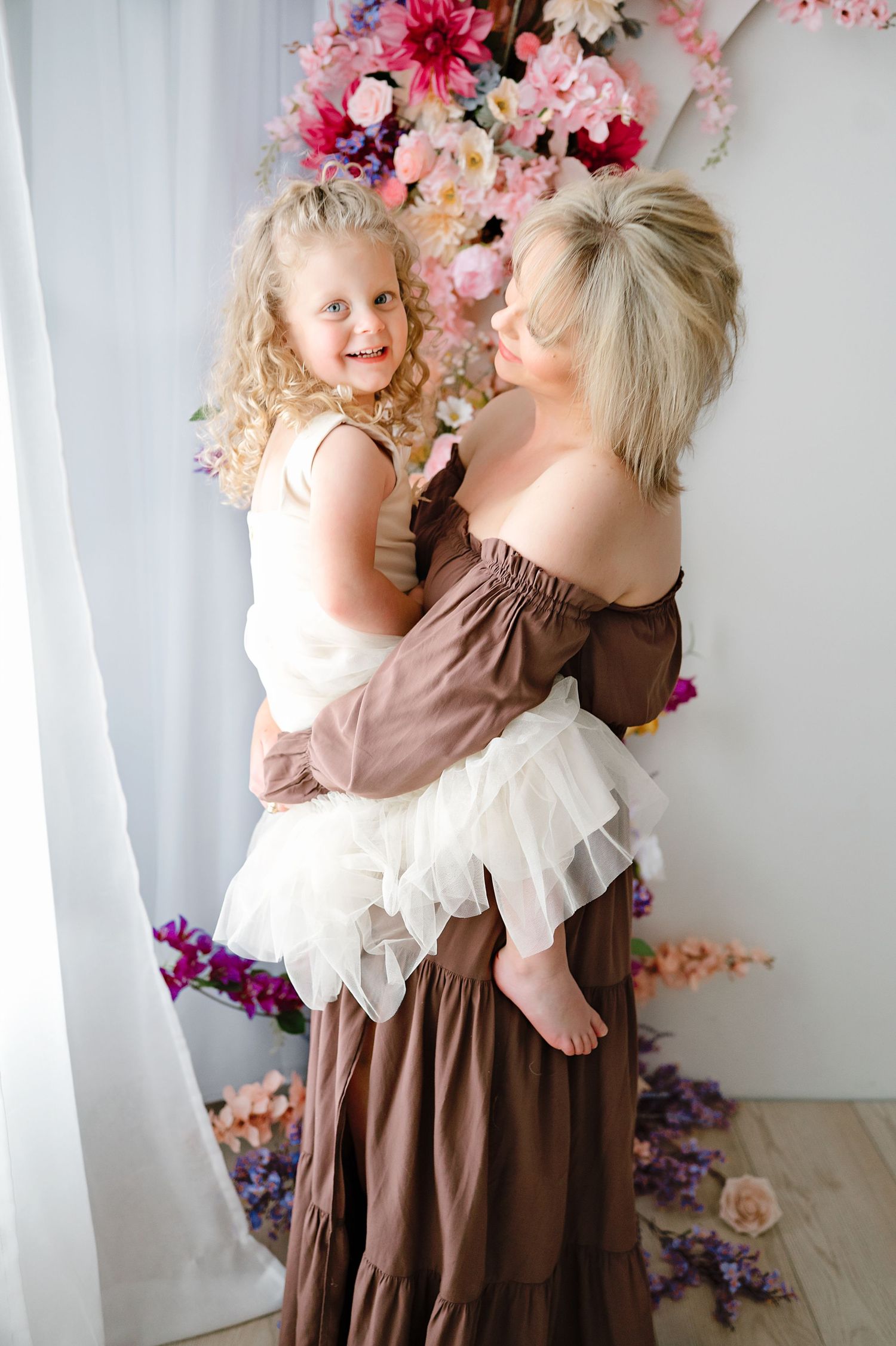 Sweet portrait moment with floral backdrop and brown maxi dress against white curtain.
