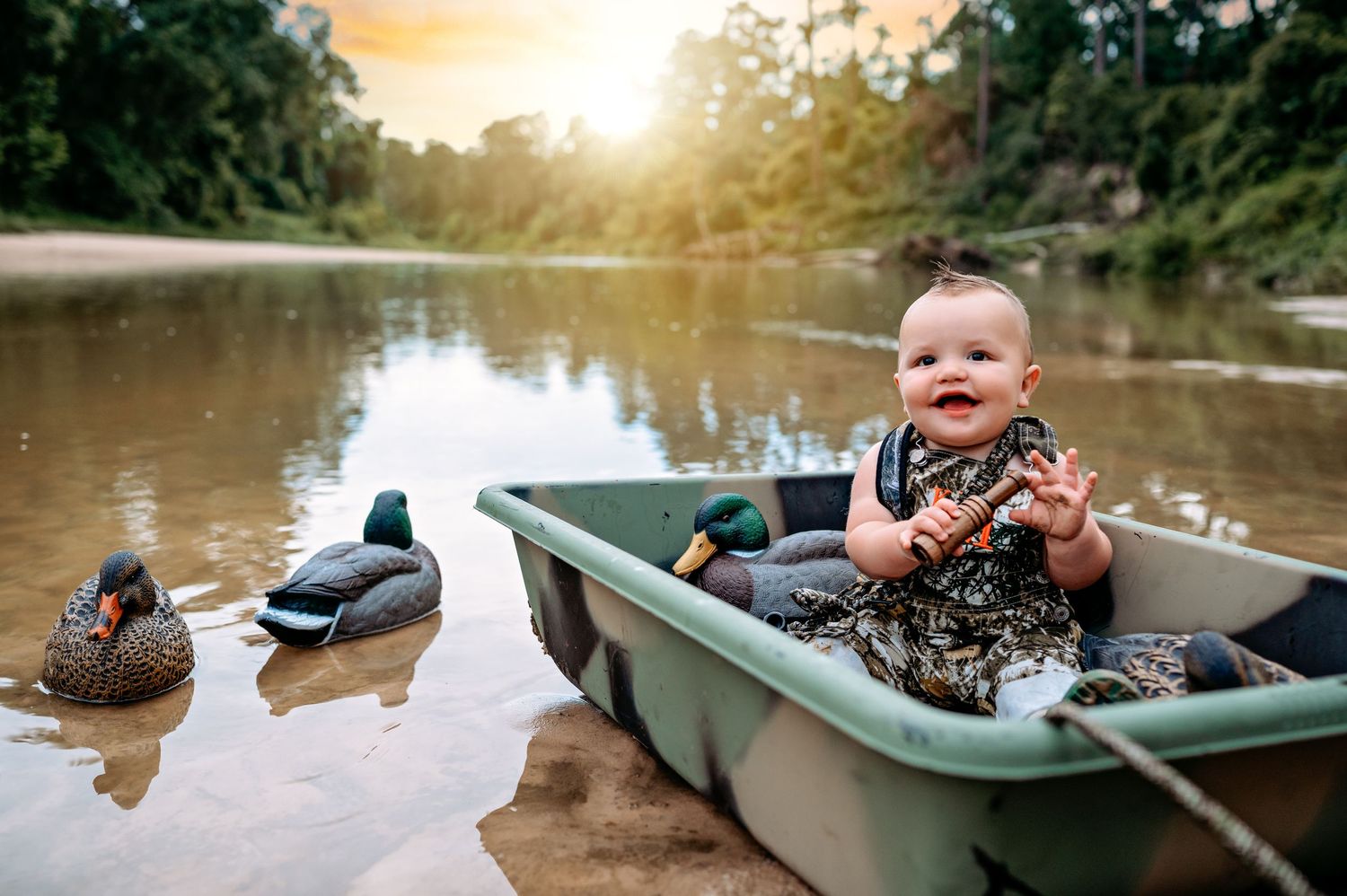 A small child sits in a canoe on a serene lake at sunset with ducks swimming nearby.