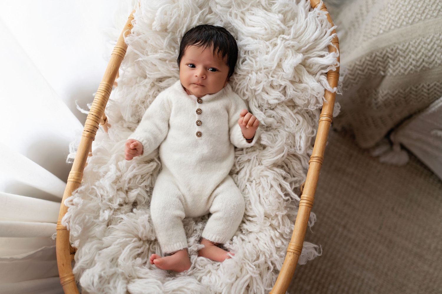 Baby wearing white outfit lying on fluffy blanket in wooden bassinet.