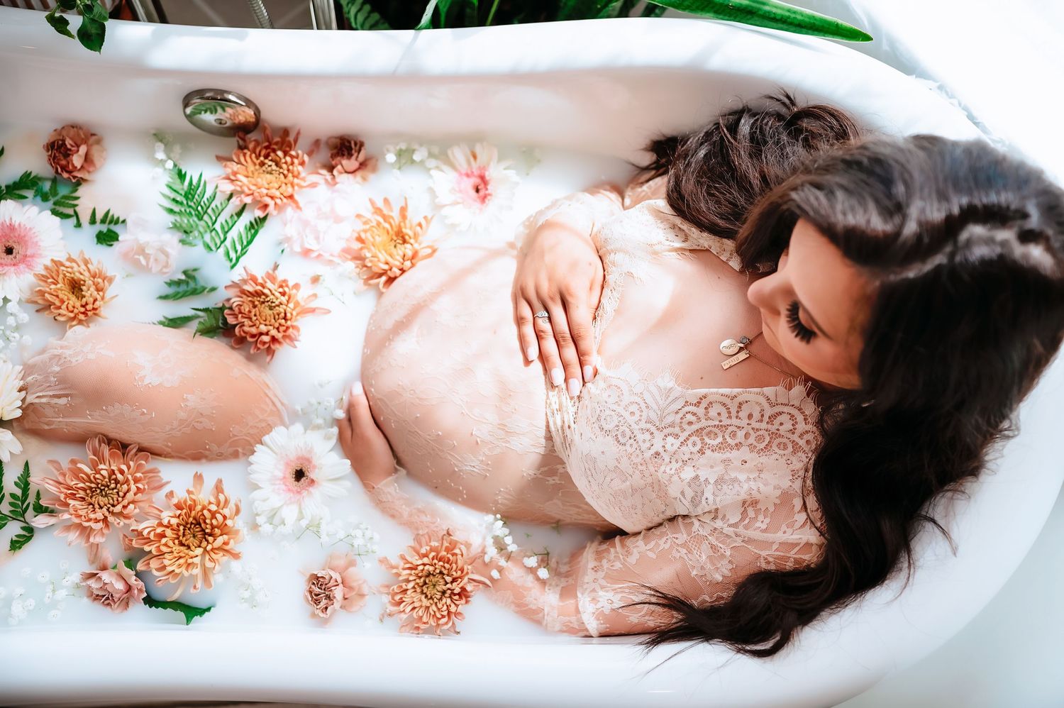 A milk bath photography session features blooming peach and coral flowers floating around a figure in white.