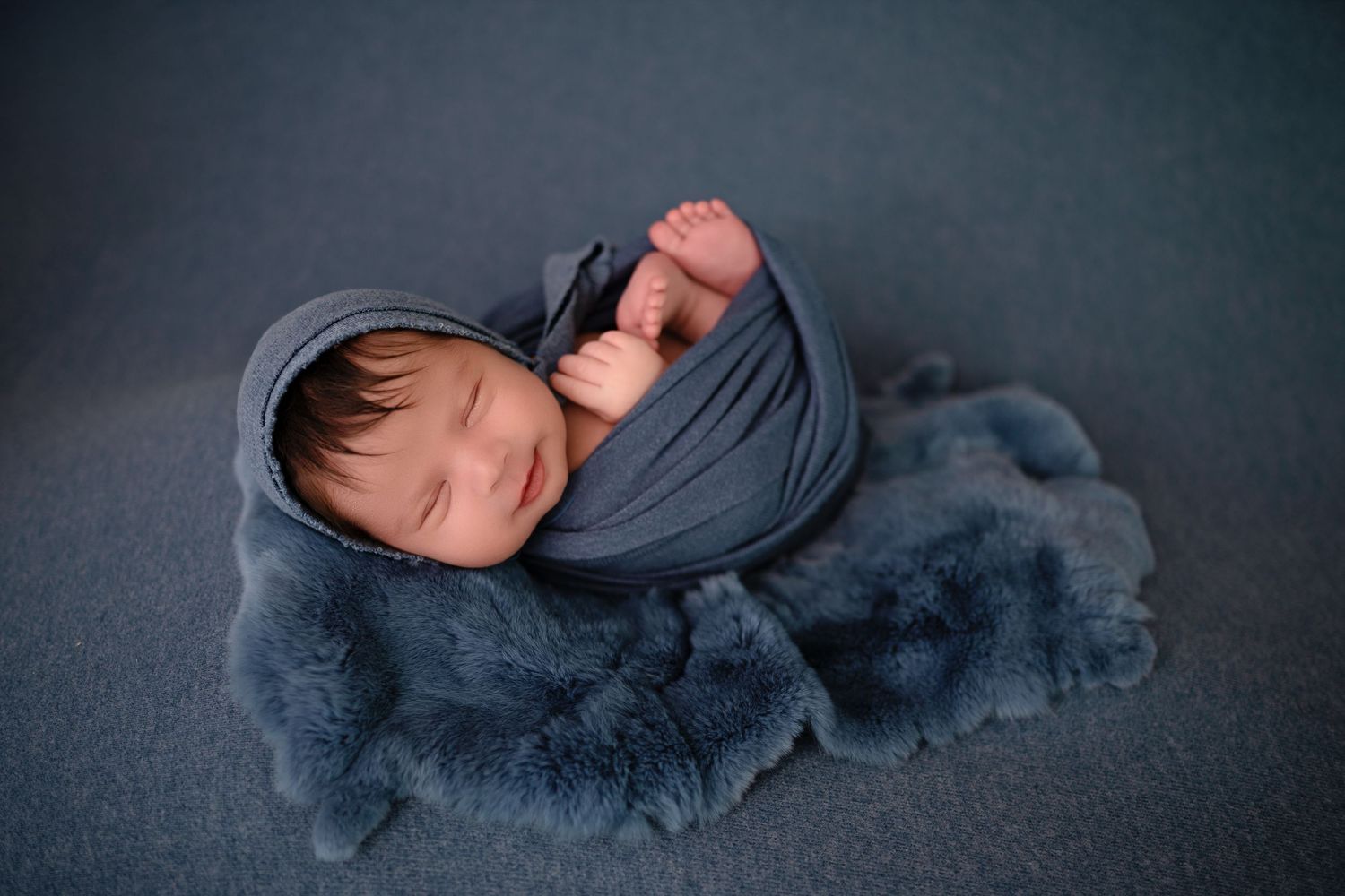 A sleeping baby lies on a dark gray blanket in a series of peaceful poses.