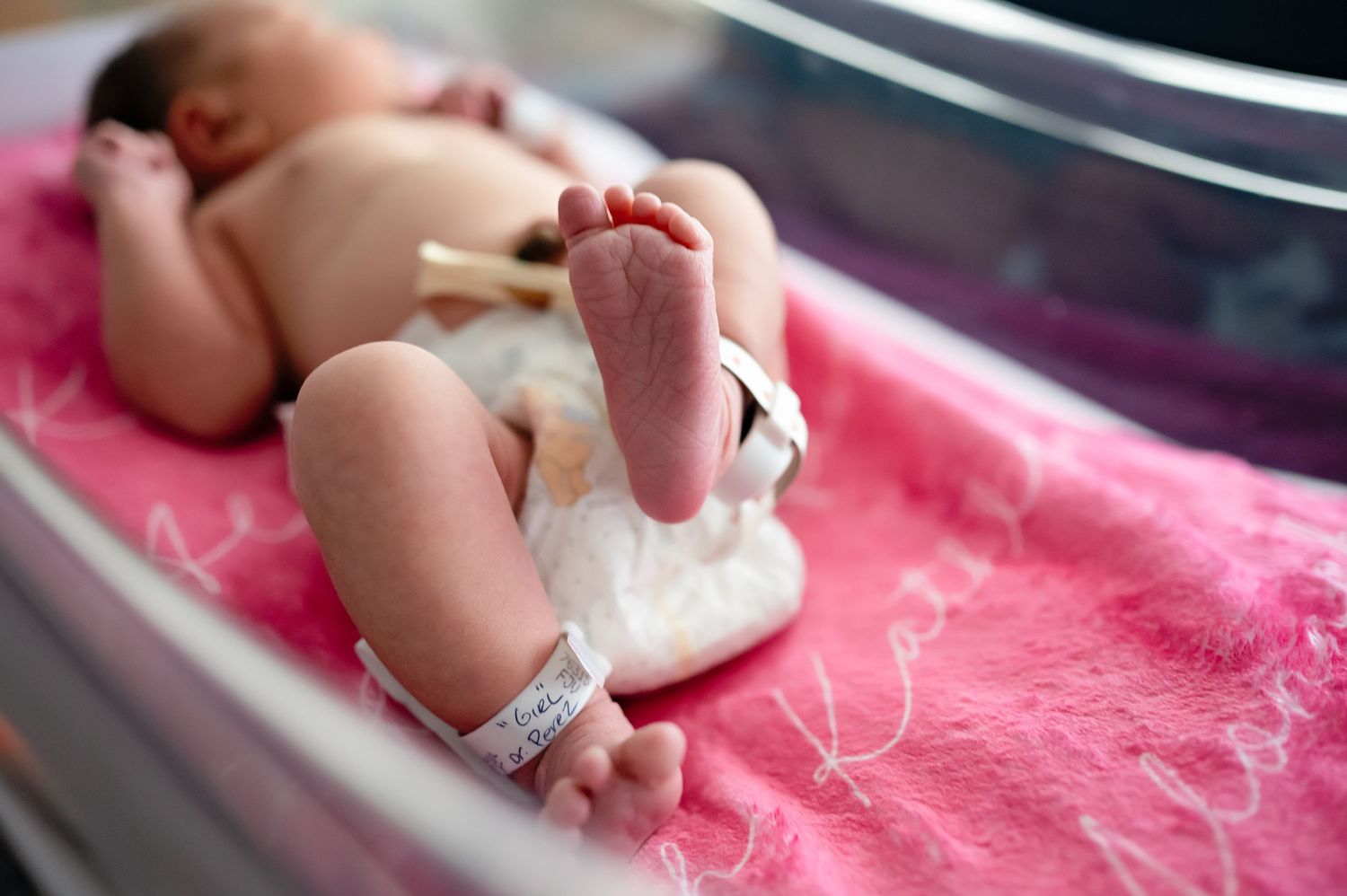 Side view of newborn baby resting on plush pink fabric during photo session.