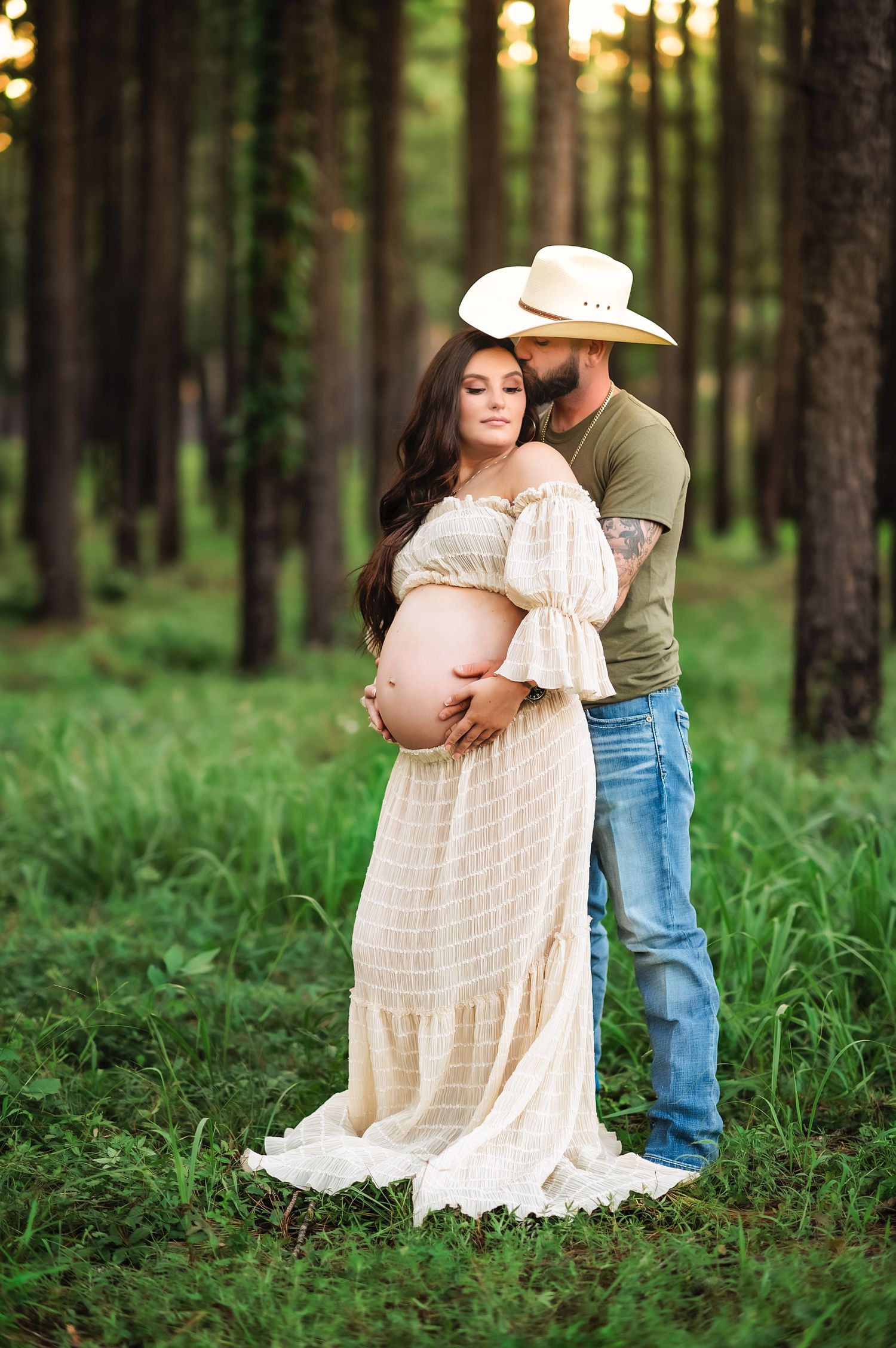 An intimate maternity portrait of a couple in a sunlit forest with pine trees.