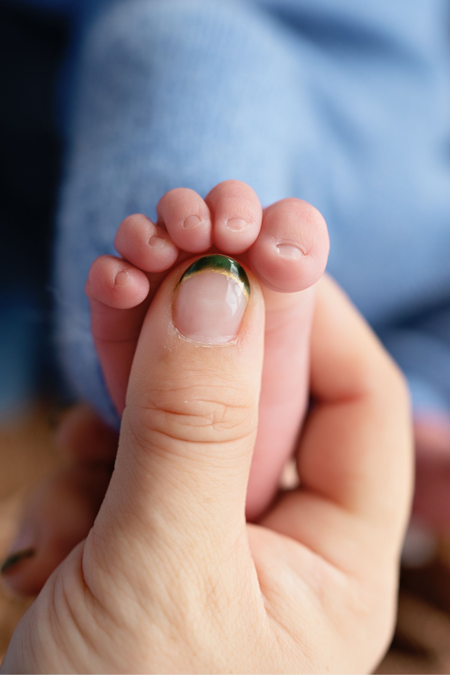 A close-up photo of a tiny baby foot being gently held against a blue background.