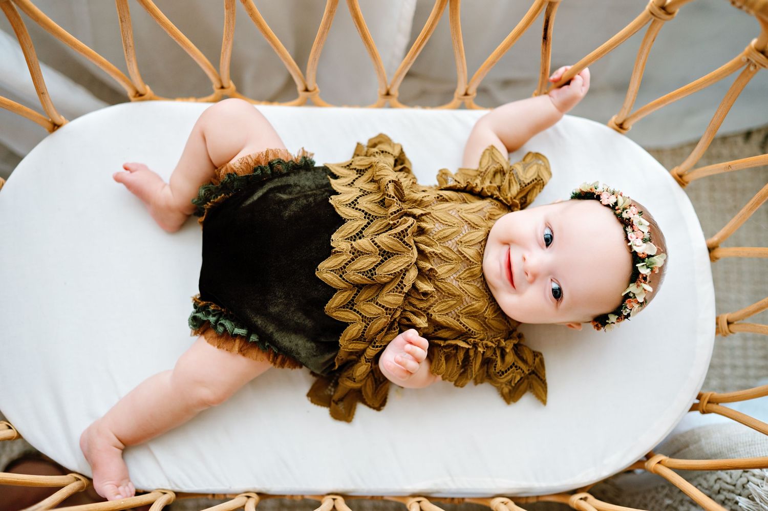 Small child wearing black and brown ruffled outfit laying on white wicker furniture.
