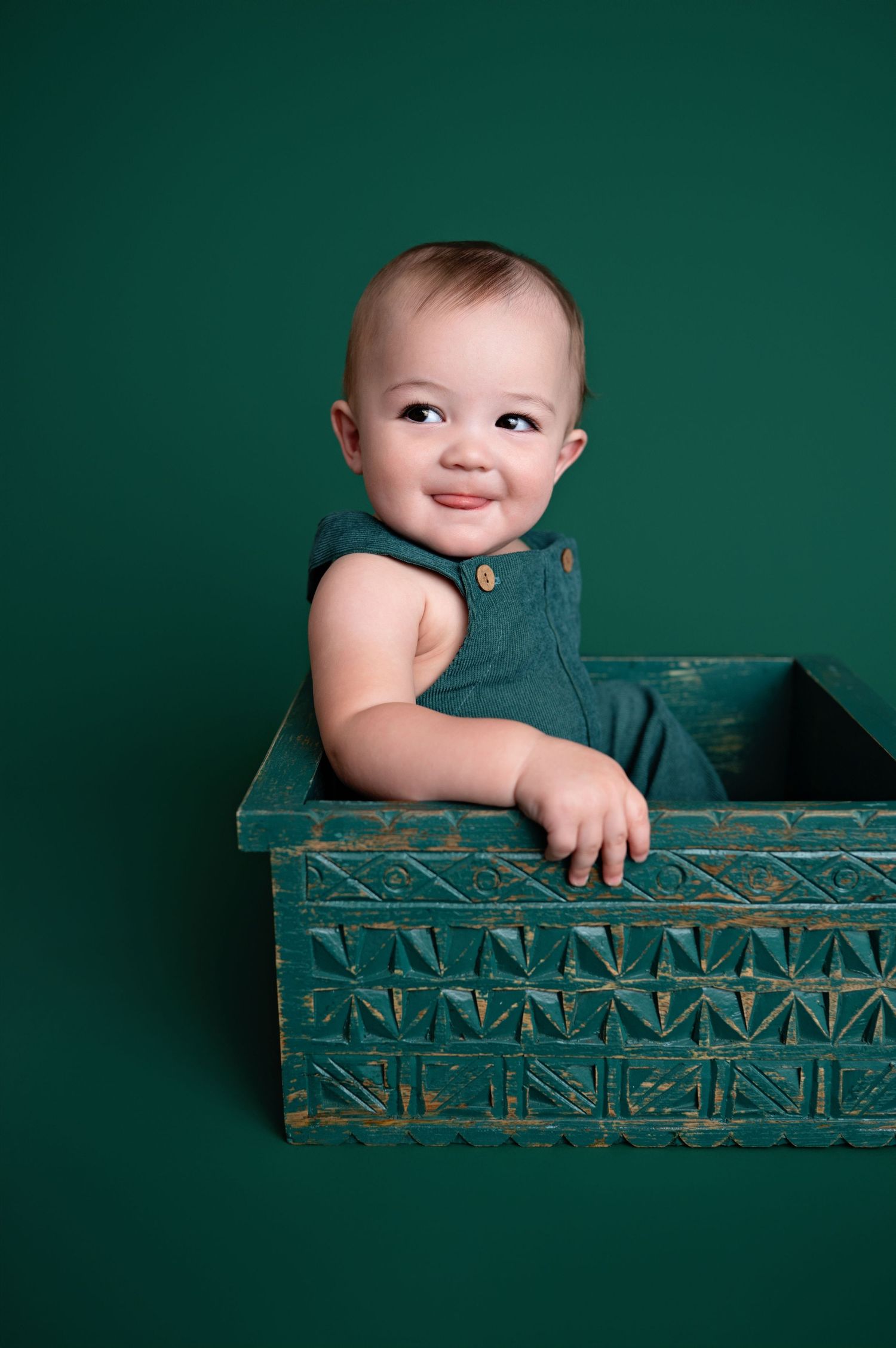 Baby poses playfully in vintage teal wooden crate against dark green background in progressive series of images.