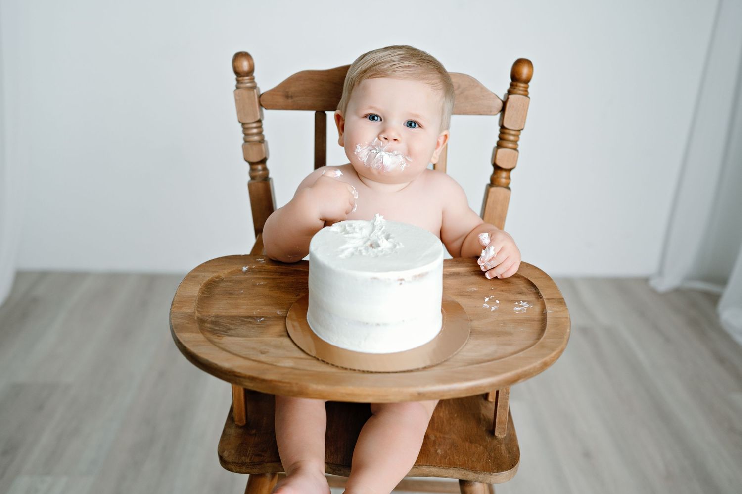 A wooden high chair with decorative spindles is set against a white wall backdrop.