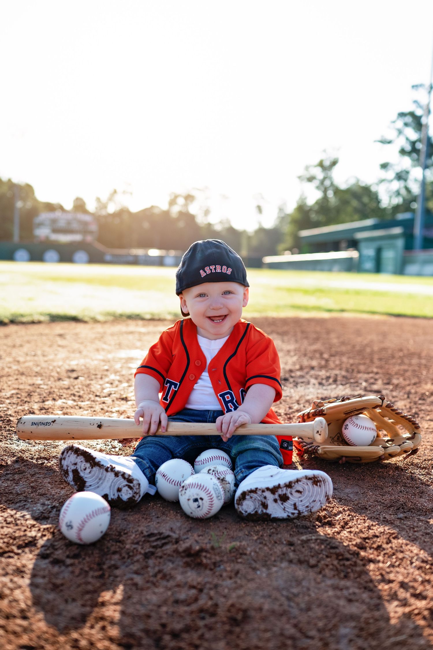Baseball gear and equipment arranged on a dirt infield with sunlit background at a baseball field.