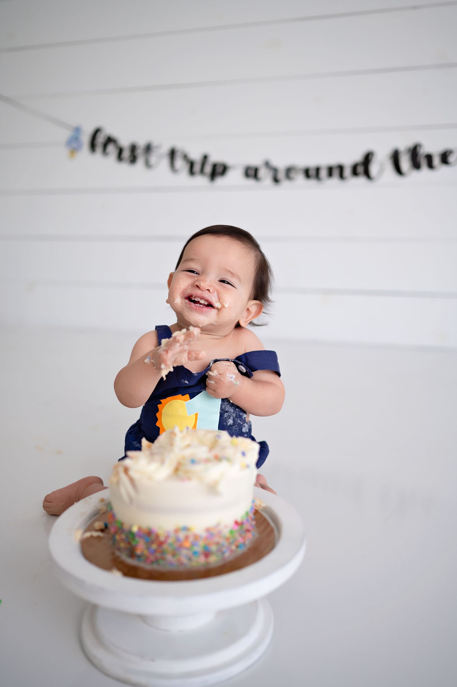 A sequence of images showing a baby's first birthday cake smash photo session with sprinkle-covered white frosted cake.