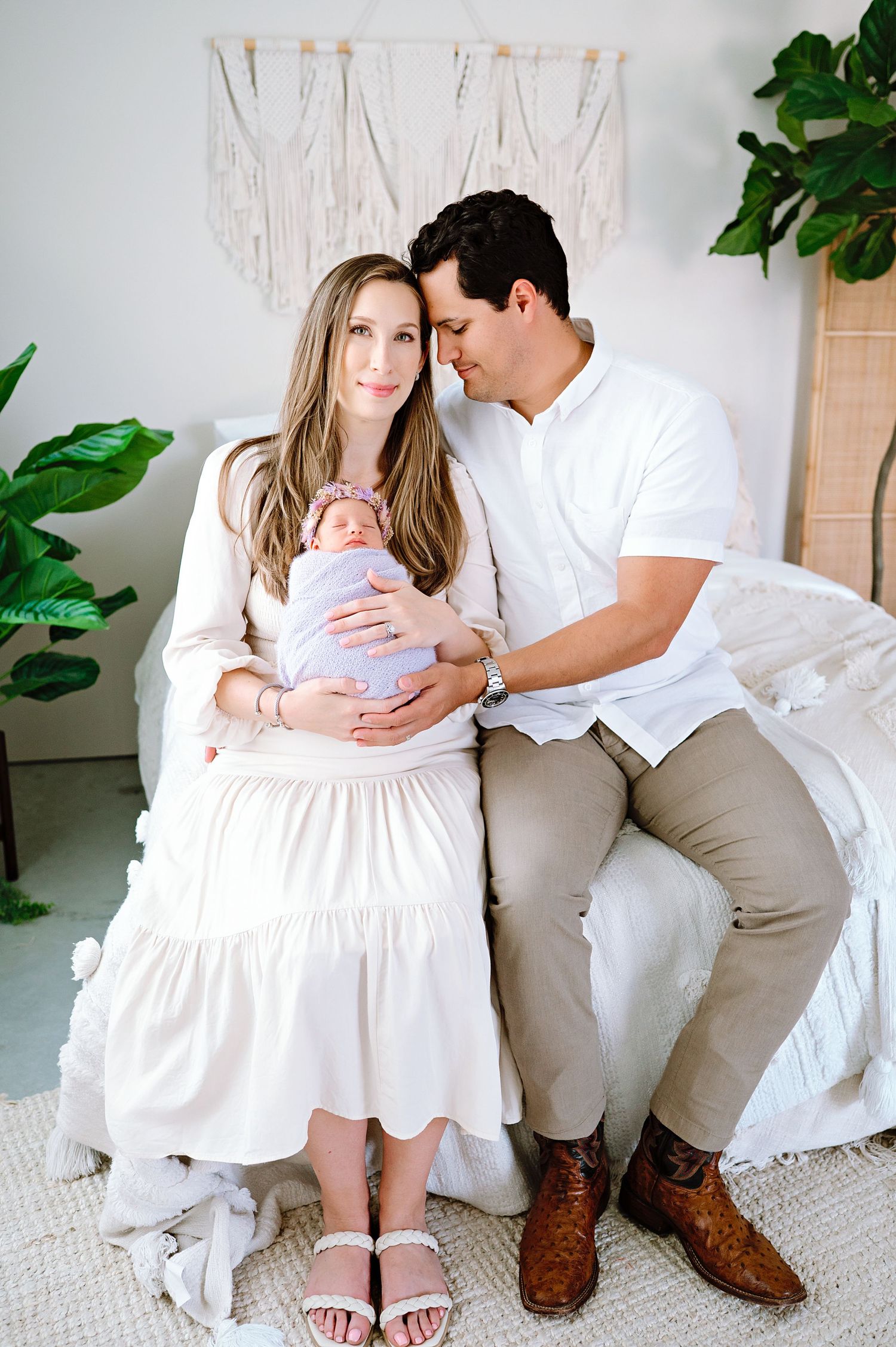 Intimate family moment on white couch with macrame wall hanging and plants.