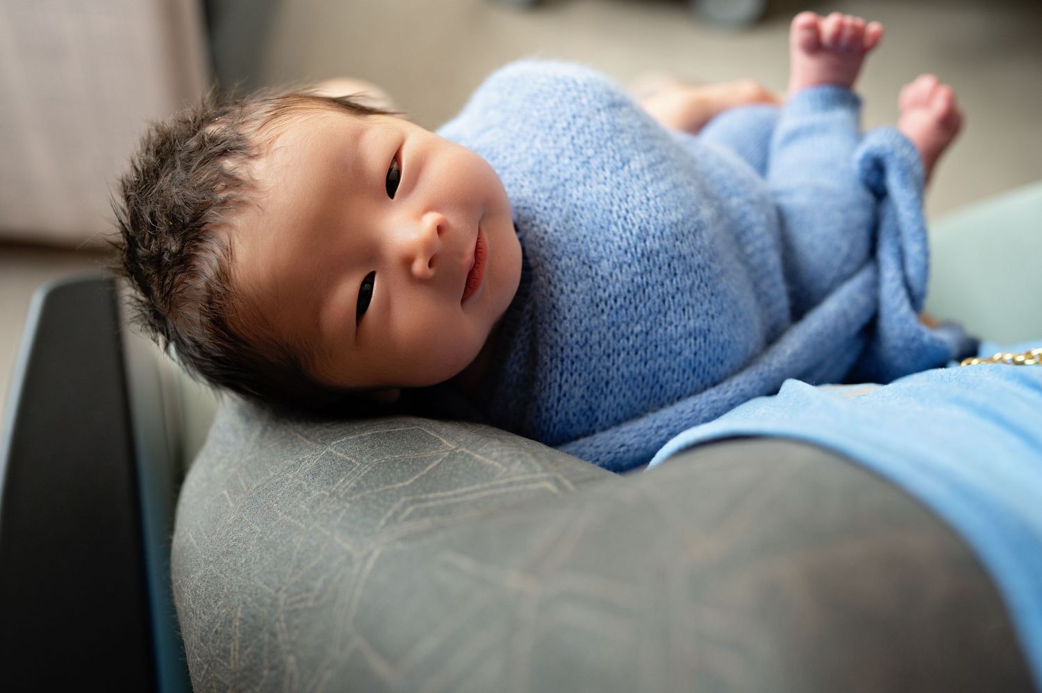 A baby wearing a blue sweater lies peacefully on a soft surface while sleeping.