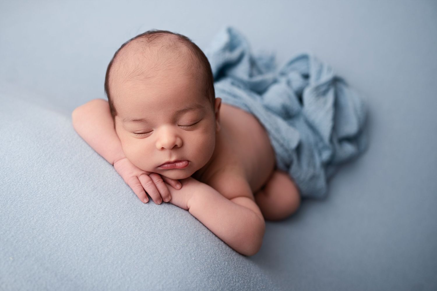 Peaceful newborn baby sleeping on a soft blue blanket with a light blue wrap, perfect newborn photography pose.