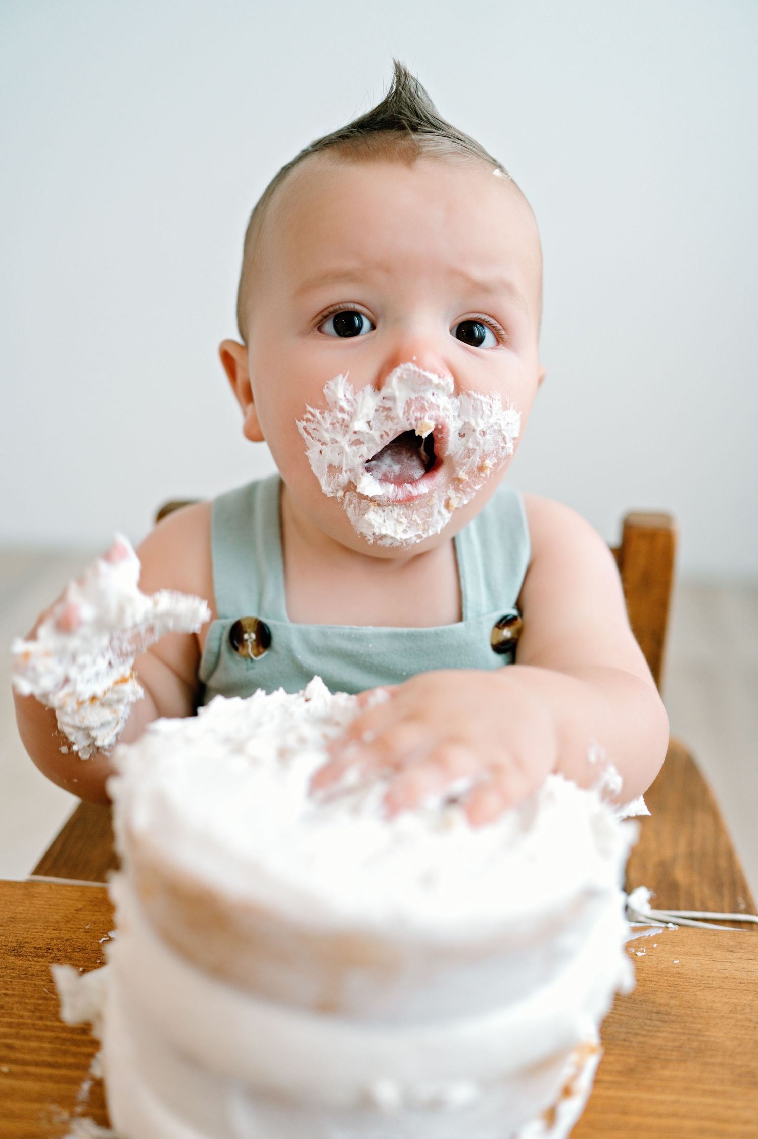A sequence of images shows a small infant making a playful mess while eating a cake, with frosting getting all over their face.