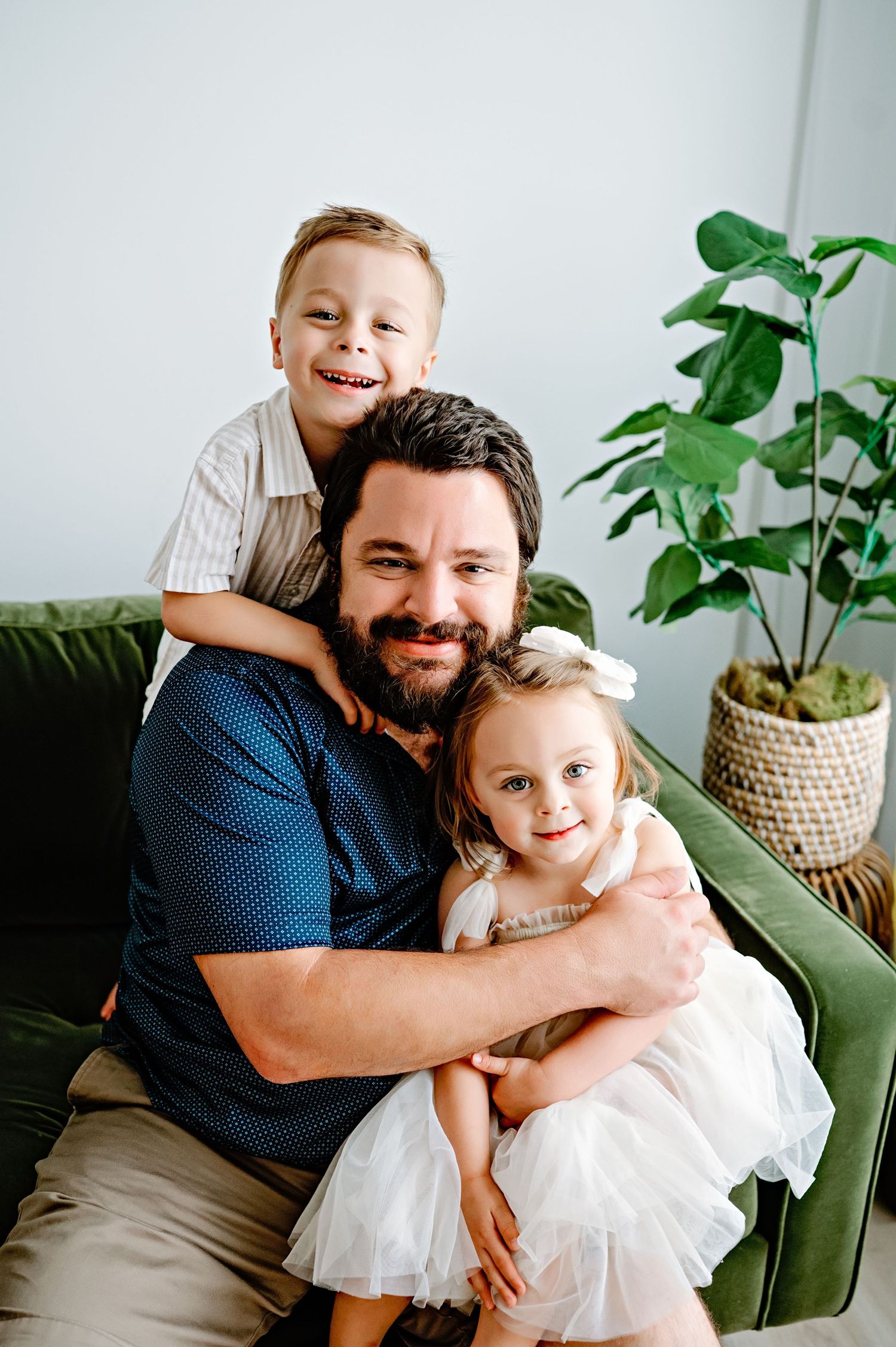 Happy family moment on green velvet couch with houseplant in background.