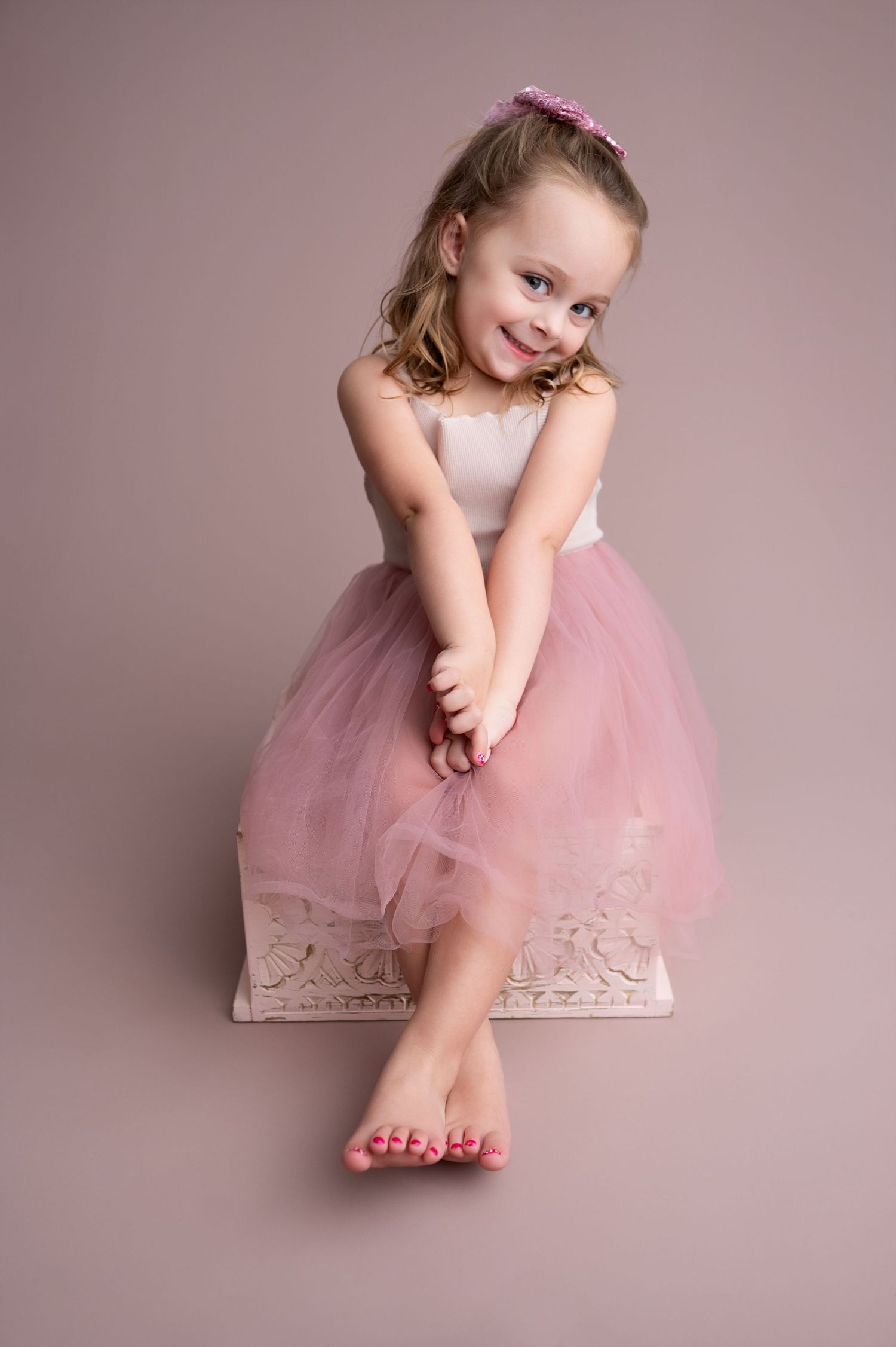 A child in a pink tulle dress poses gracefully on a cream-colored backdrop in a series of connected portraits.