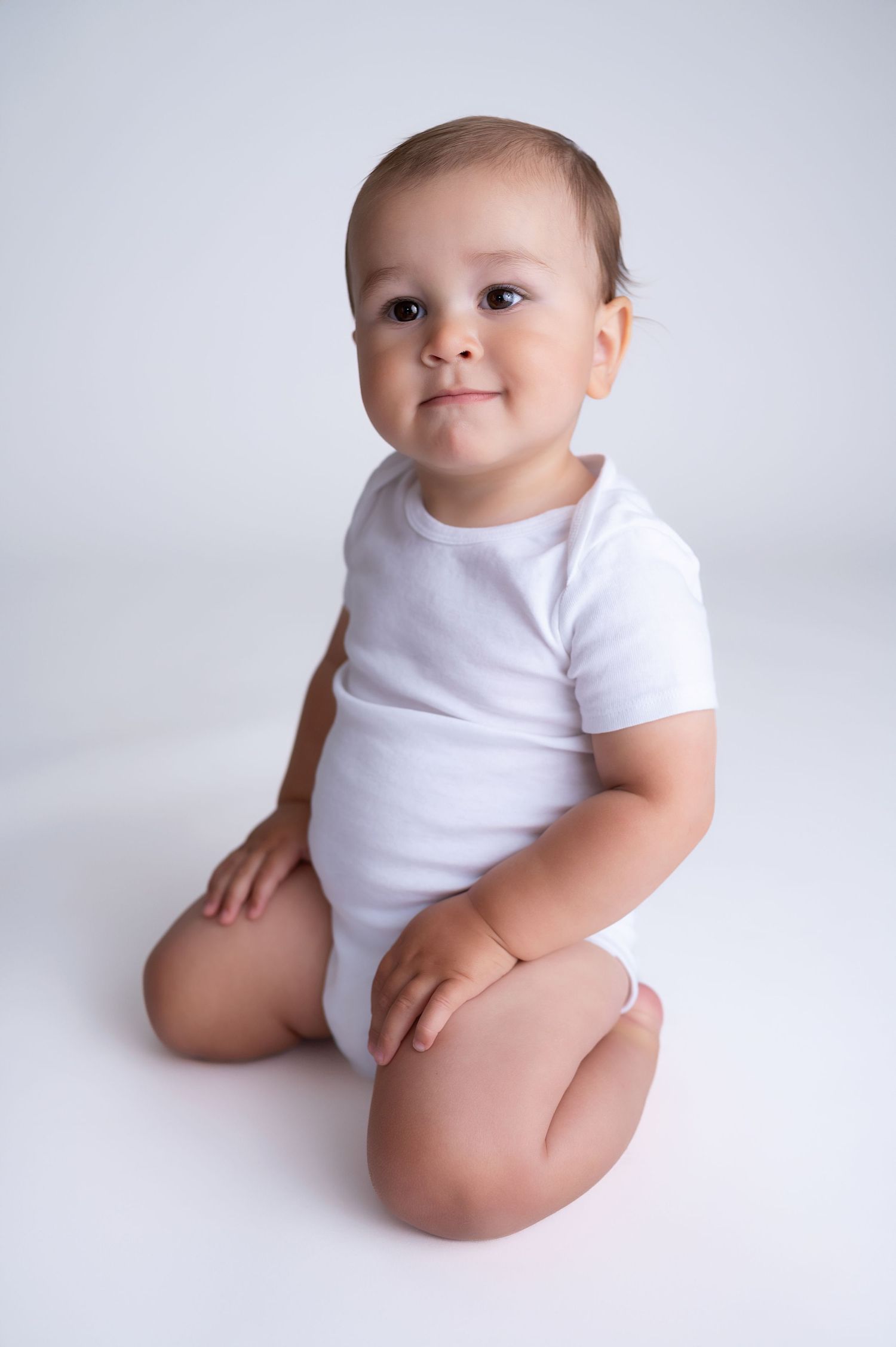 Infant wearing white bodysuit poses during minimalist photo session.