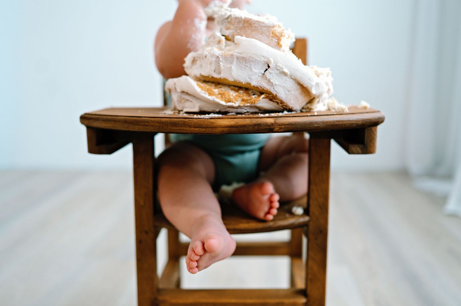 A close-up view of a childs bare feet dangling from a wooden high chair during mealtime.