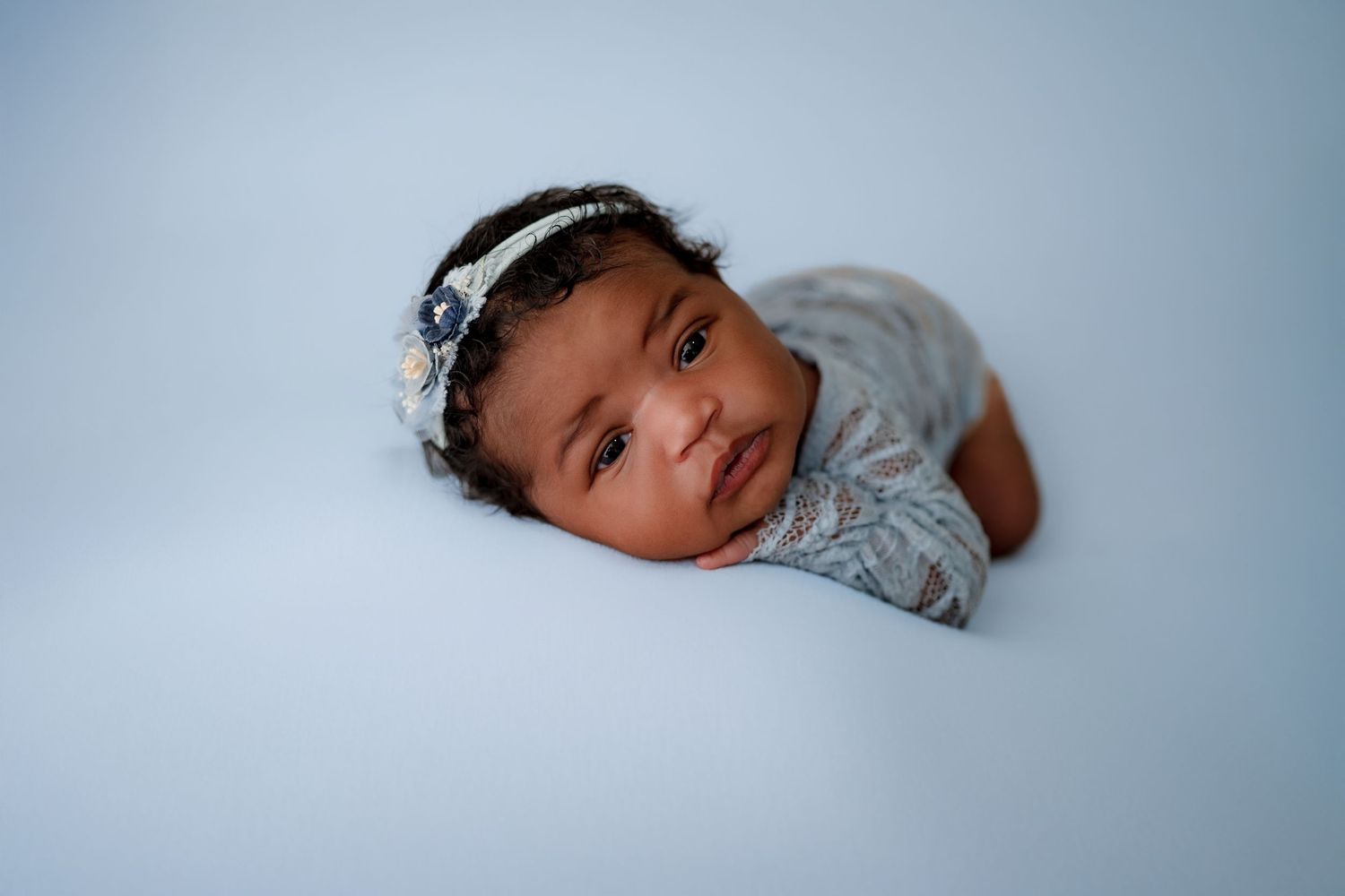 A sleeping baby wearing a gray onesie rests peacefully against a light blue background.