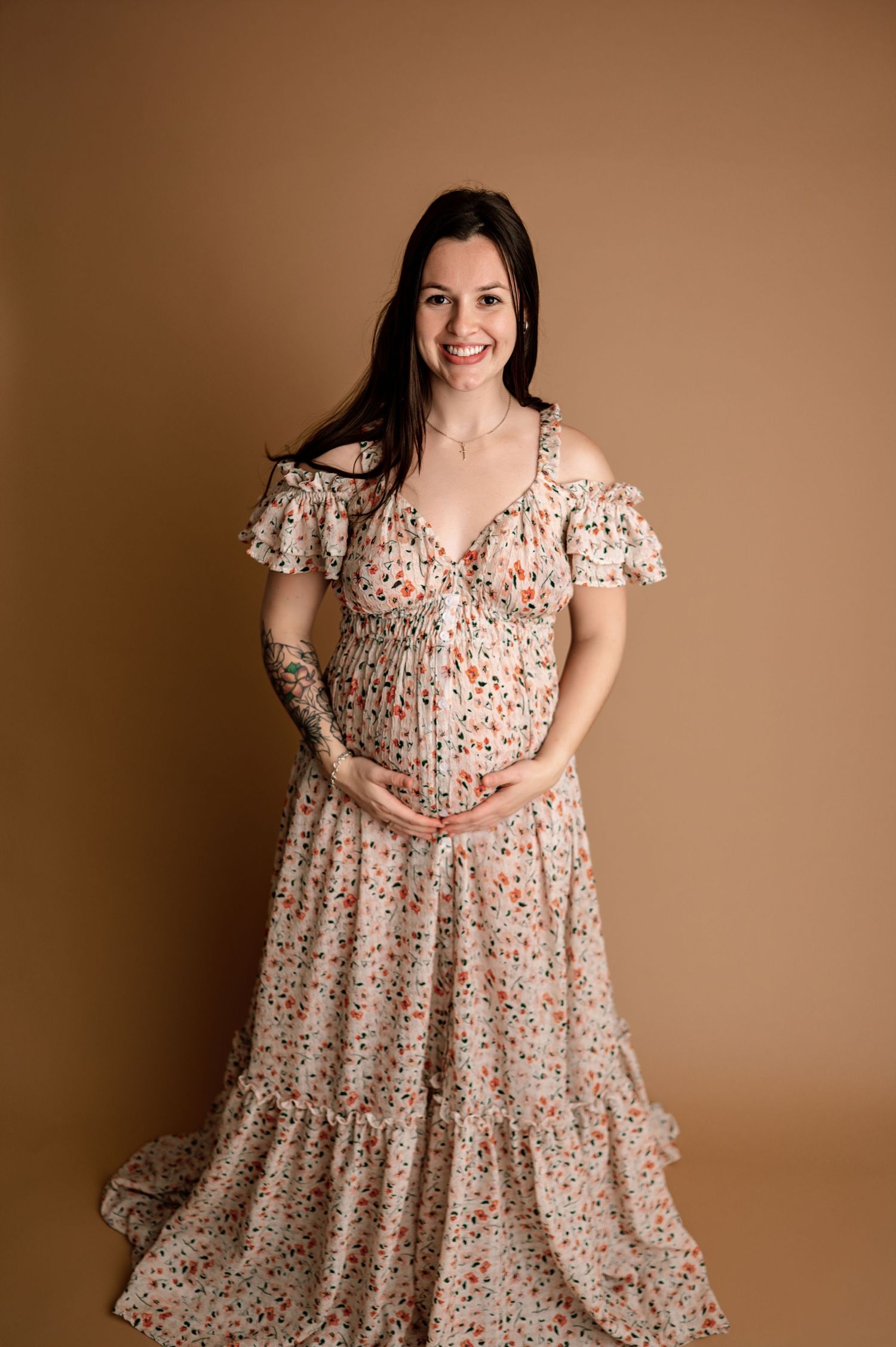 A floral print maxi dress with cold shoulder design and tiered skirt is showcased against a warm brown backdrop.