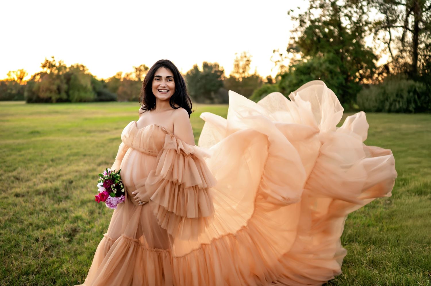 A flowing peach-colored dress billows gracefully in the wind against a sunlit grassy field at golden hour.