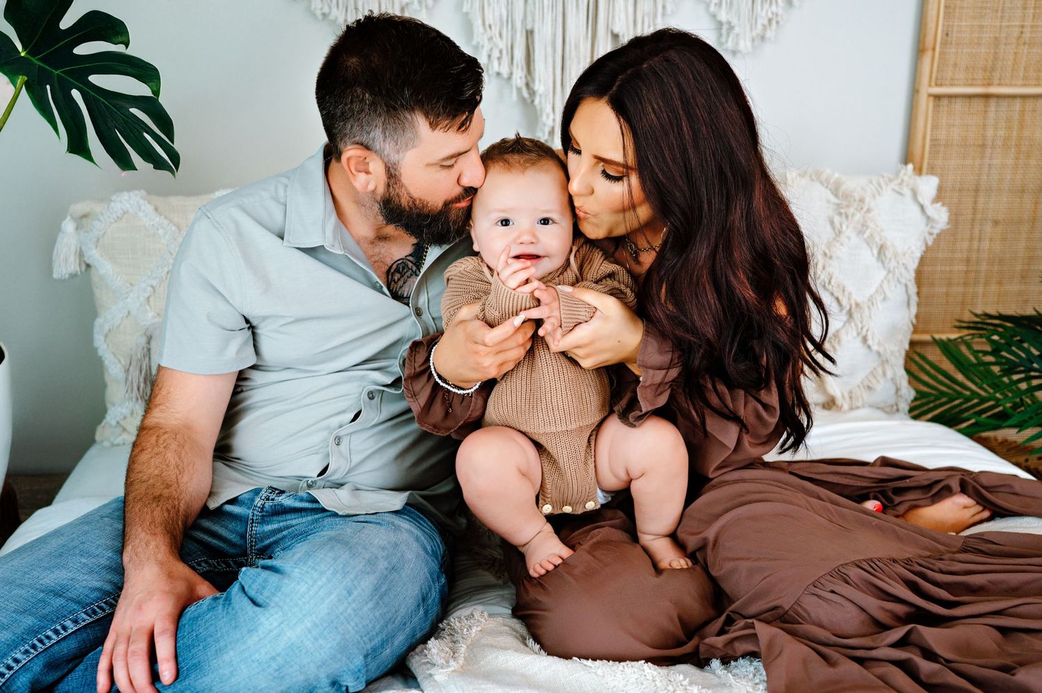 A family shares a tender moment together while sitting on a white couch with decorative greenery in the background.