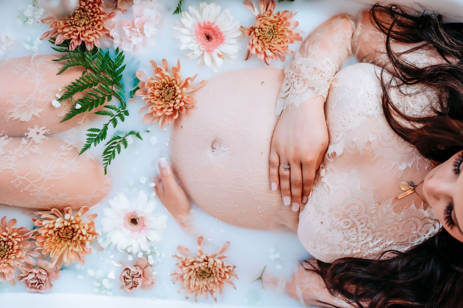 An artistic overhead view of a milk bath maternity session with orange chrysanthemums and pink flowers.