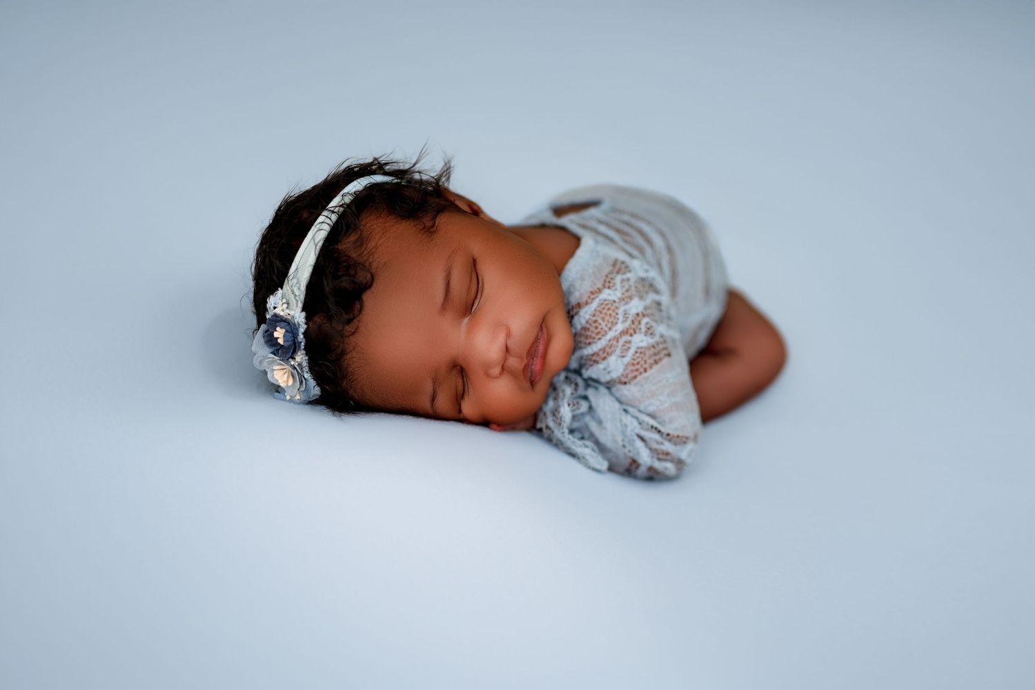 A sleeping newborn baby wearing gray clothing lies peacefully on a light blue blanket in a professional photo shoot.