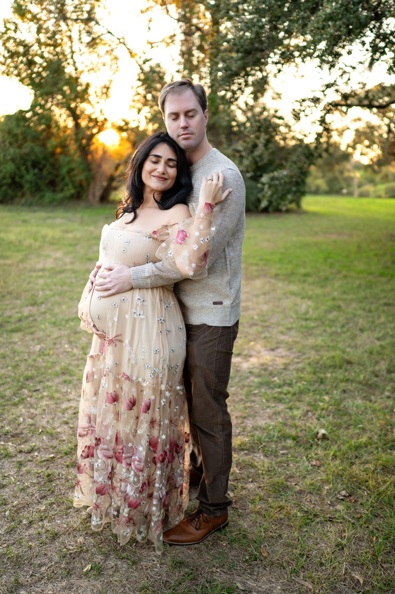 A couple embraces on grassy field during golden hour sunset in romantic outdoor photoshoot.