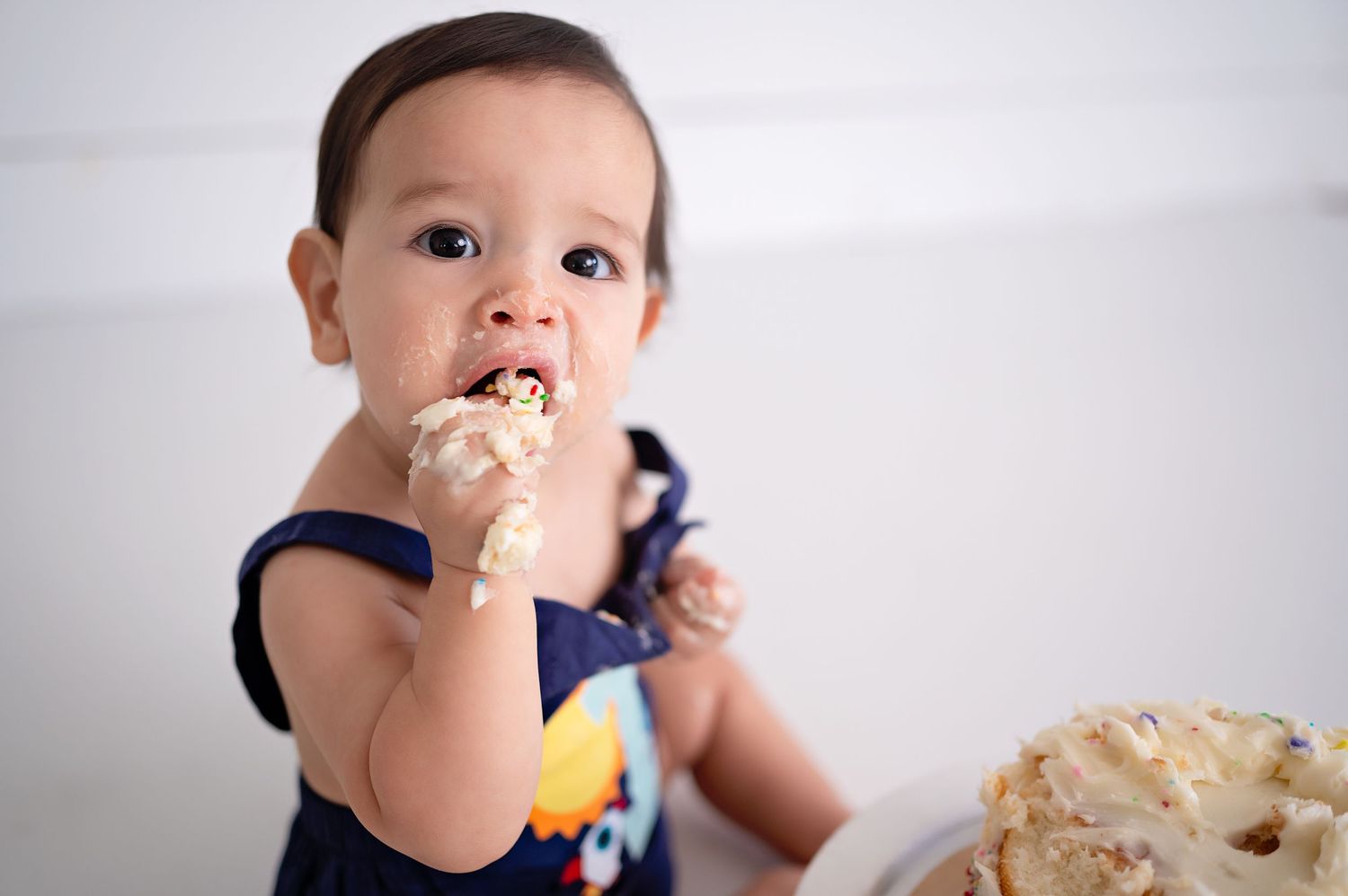 A baby in a dark shirt enjoys licking an ice cream cone while holding a juice box.