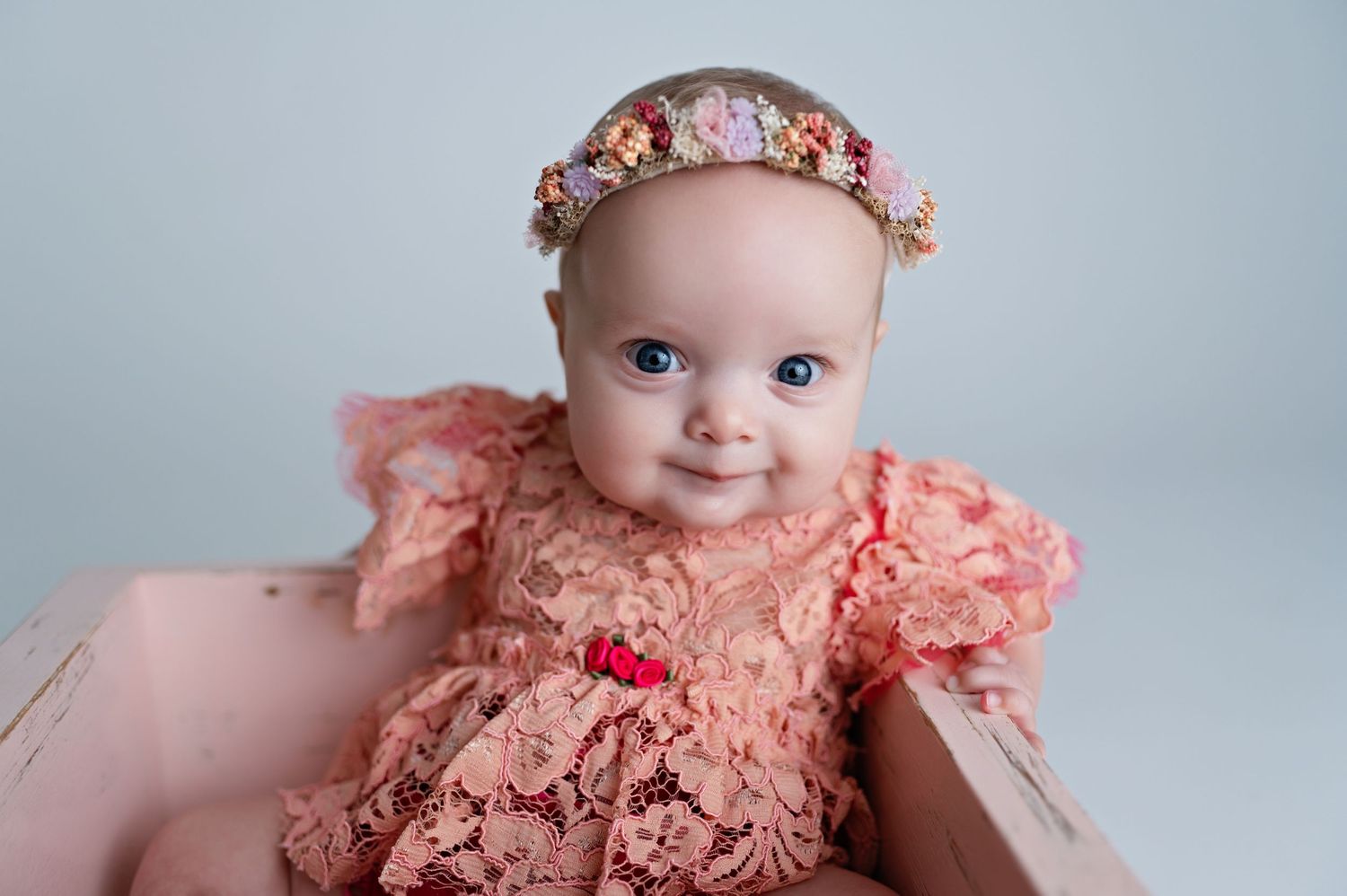Sweet baby wearing a peach lace dress and floral crown headband poses for a portrait session.