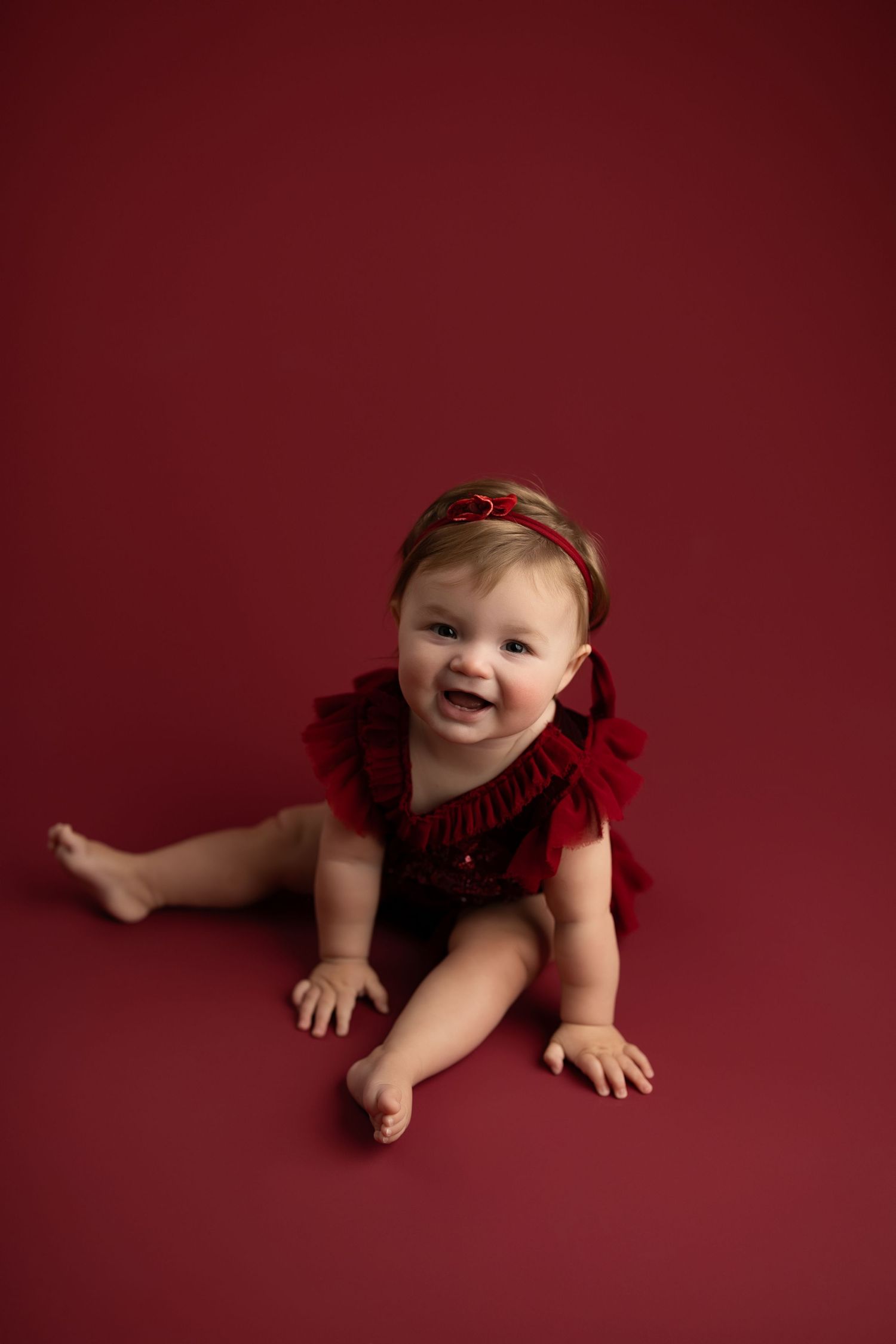 Baby in red outfit crawls and smiles against burgundy backdrop in progression of connected photos.