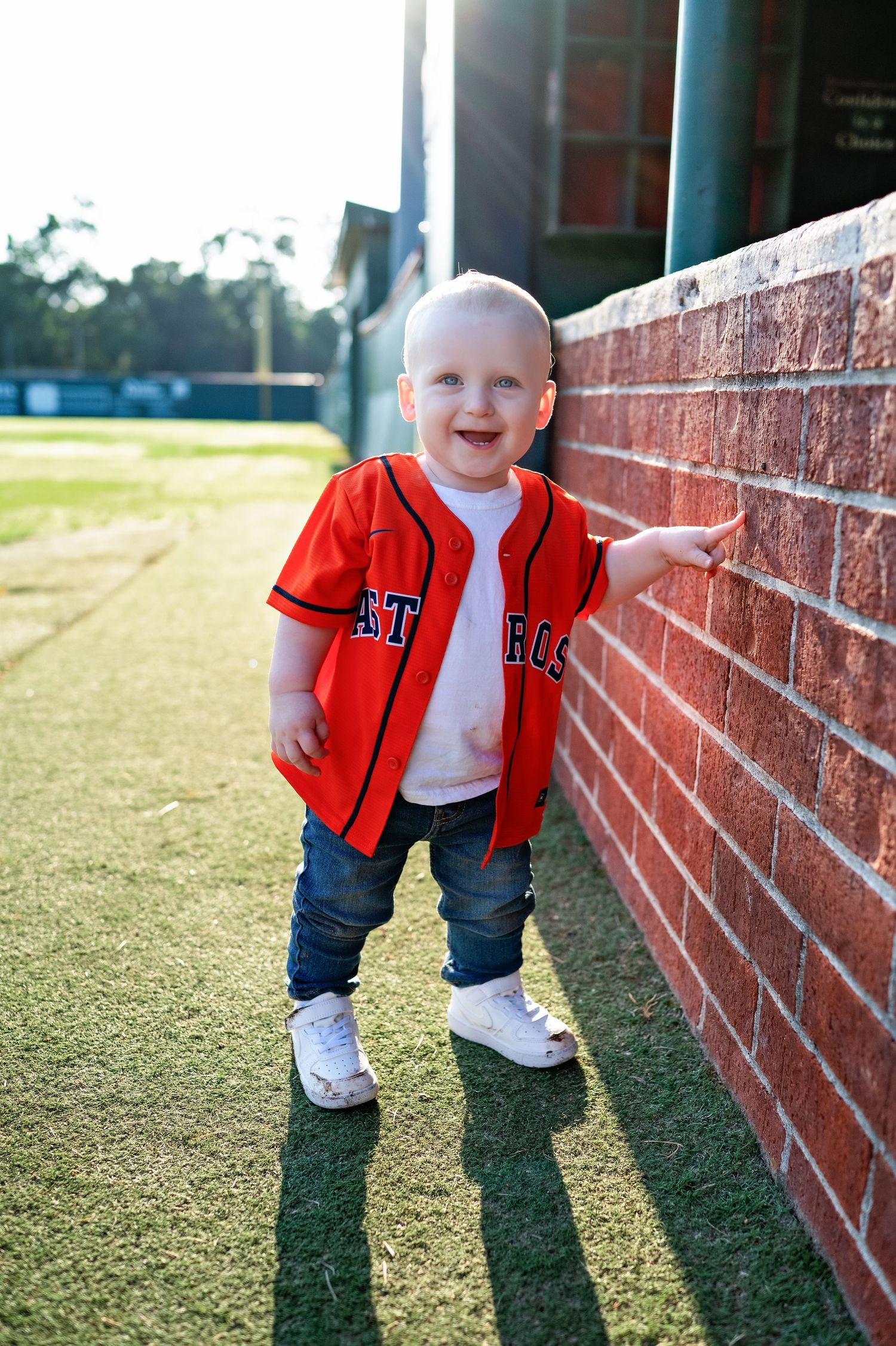 A red baseball jersey against a brick wall backdrop at a baseball field during golden hour.
