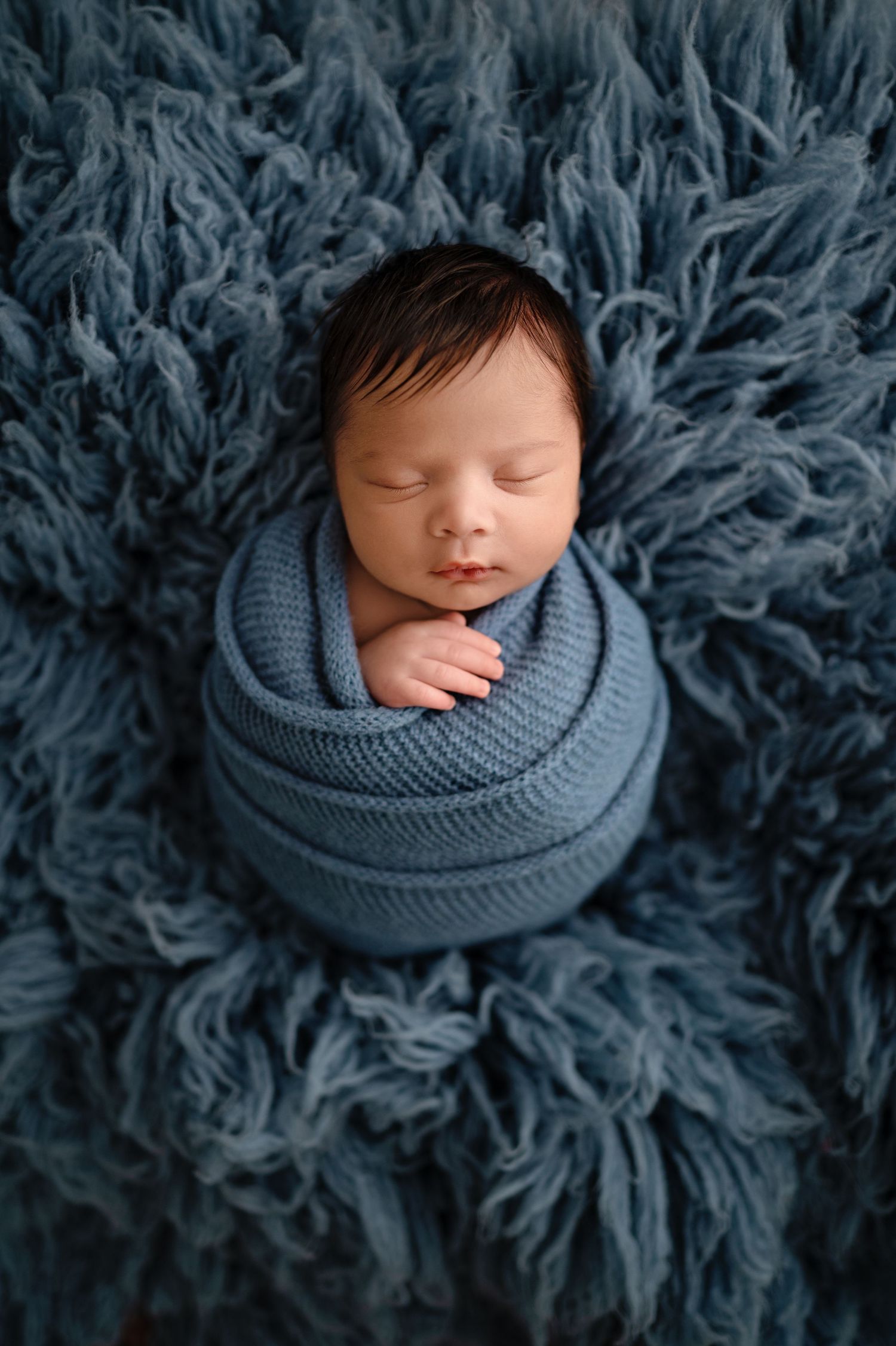 A peaceful newborn nestled in cozy gray knit fabric on a textured gray background.