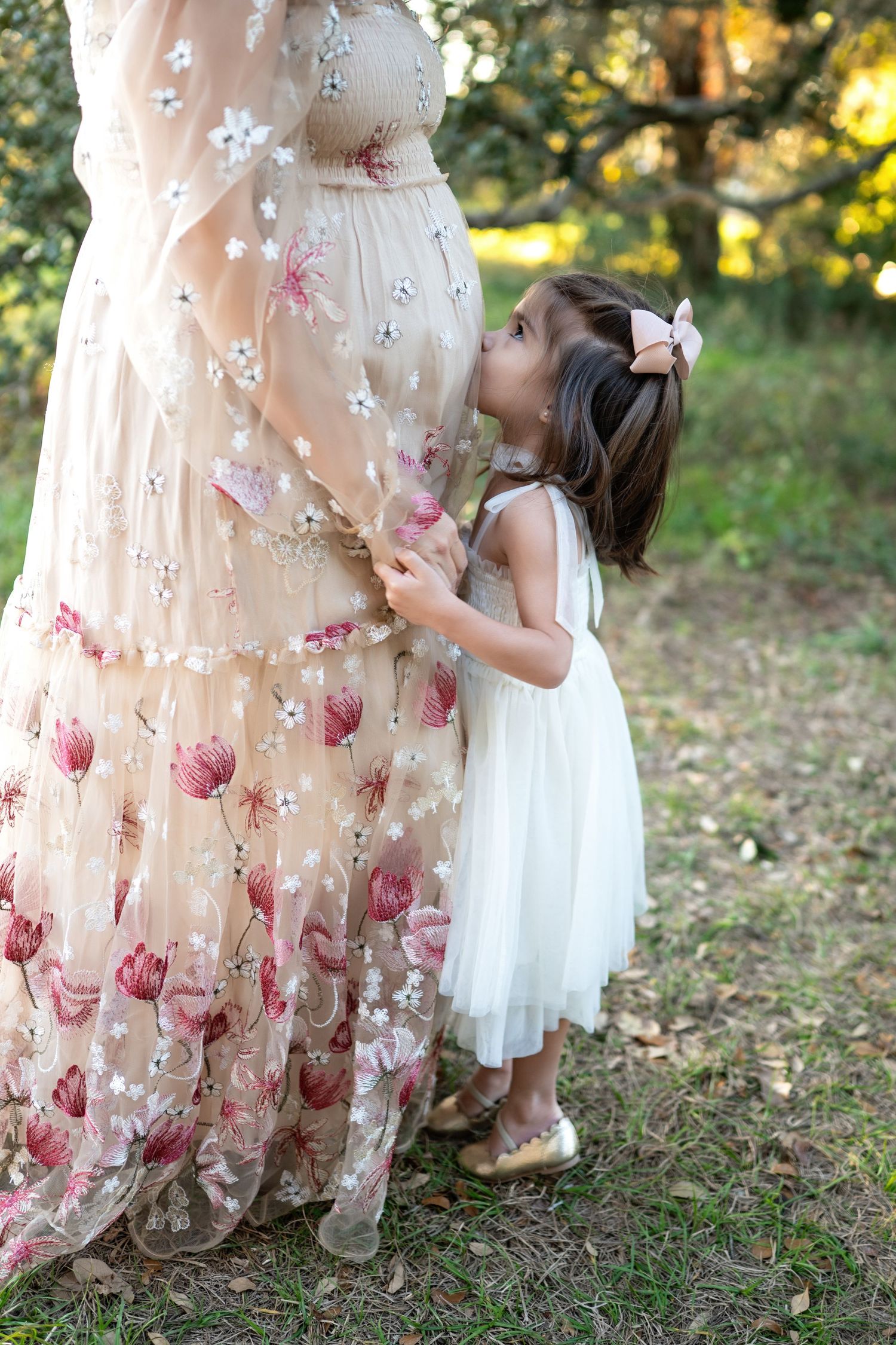 A delicate floral embroidered dress is shown alongside a white tulle dress in an outdoor garden setting.