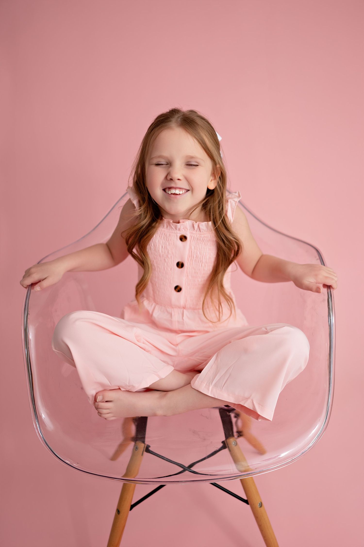 Four sequential photos show a young child in pink clothing sitting playfully in a clear modern chair against a pink backdrop.