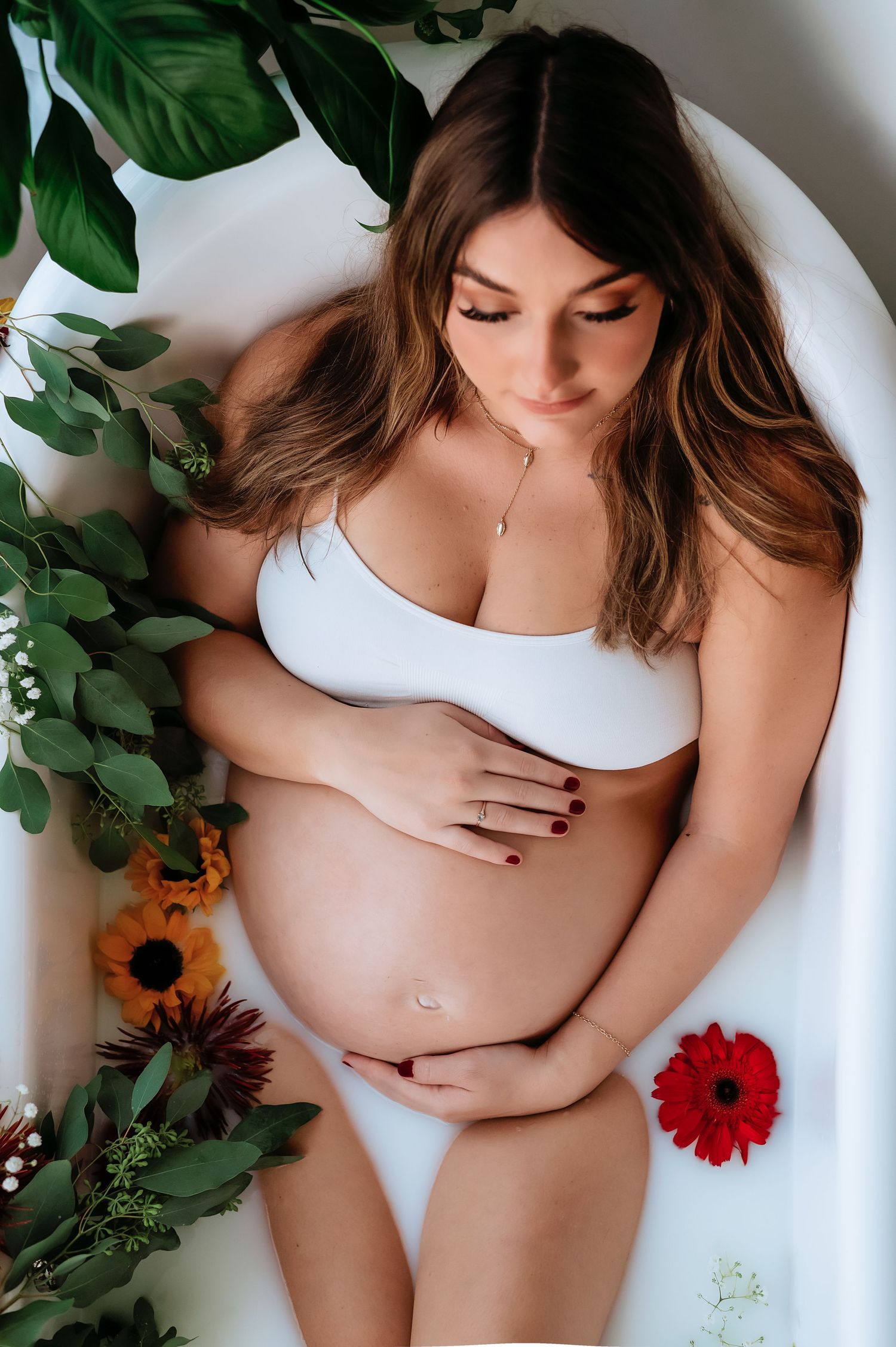 A serene maternity milk bath photo featuring sunflowers and red gerbera daisies with tropical leaves.