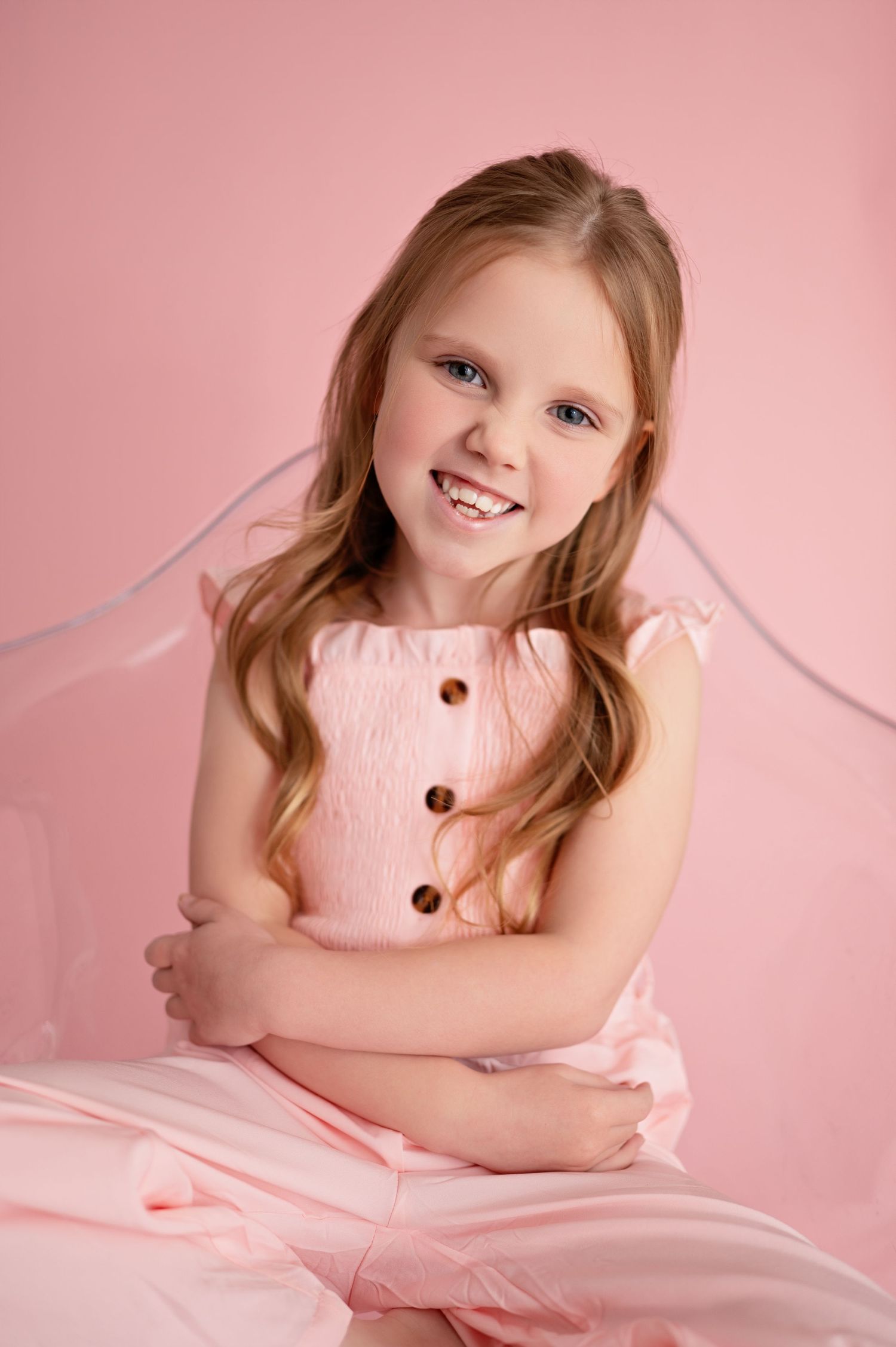 Child in pink dress poses against pink background in sweet portrait series.