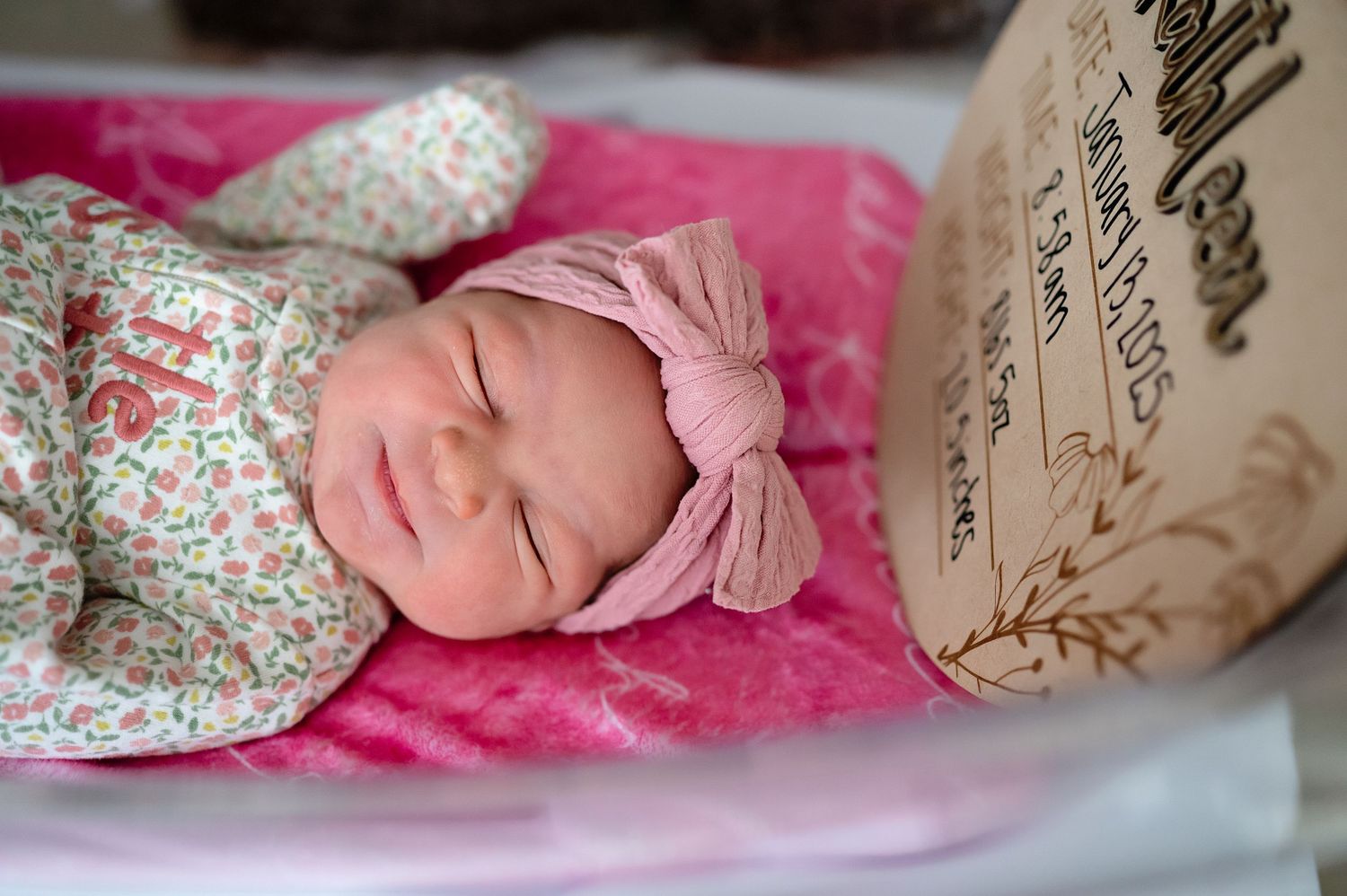 Artistic newborn photography with baby in floral outfit on pink backdrop.