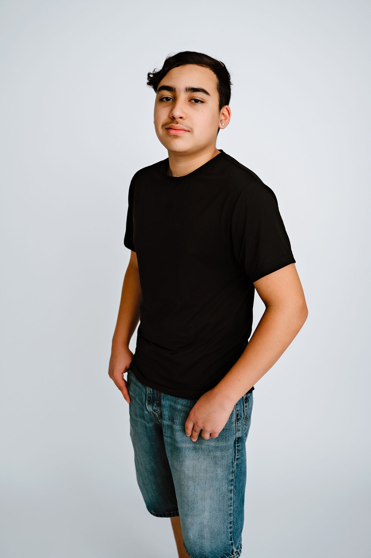 A teen boy in a black t-shirt and jeans poses against a white backdrop.