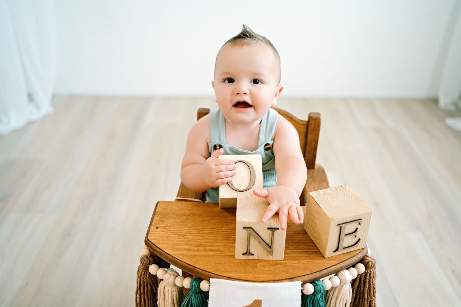 Baby sits at wooden table with alphabet blocks during first birthday cake smash photo session.