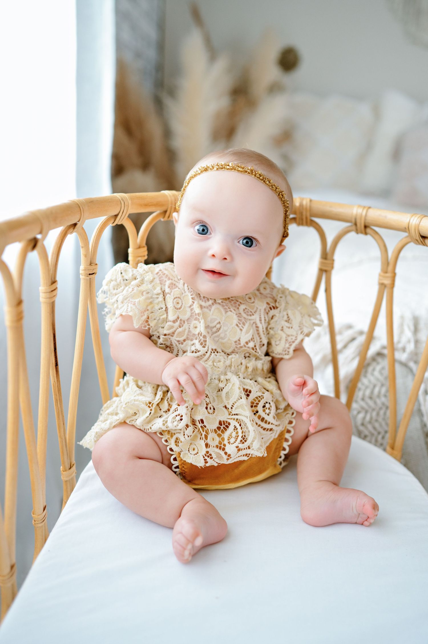 Baby wearing gold lace dress sits on rattan bench with white cushion in sequence of progression photos.