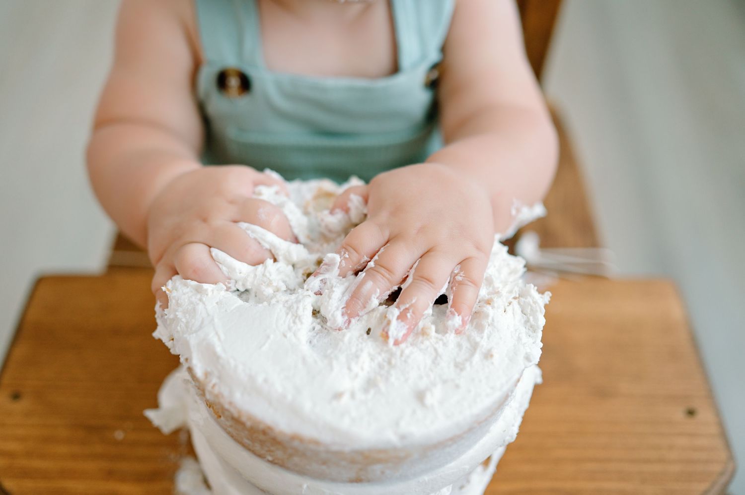 Small hands press dough into a white floured bowl on a wooden table.
