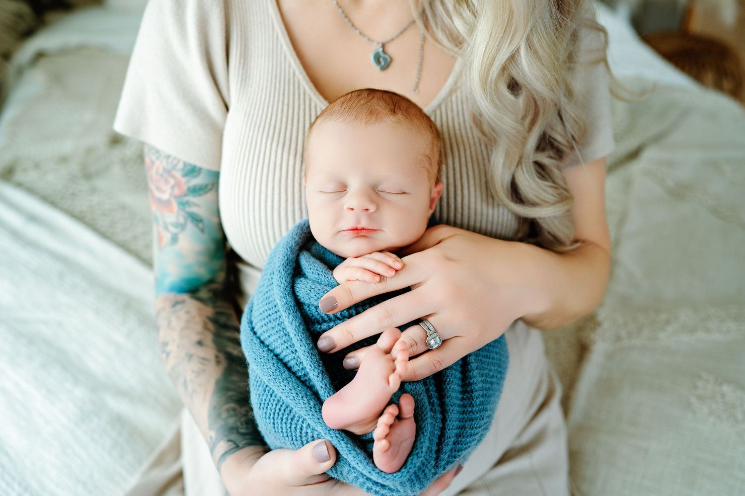 A newborn baby wrapped in blue blanket rests against white bedding while being held gently in arms.